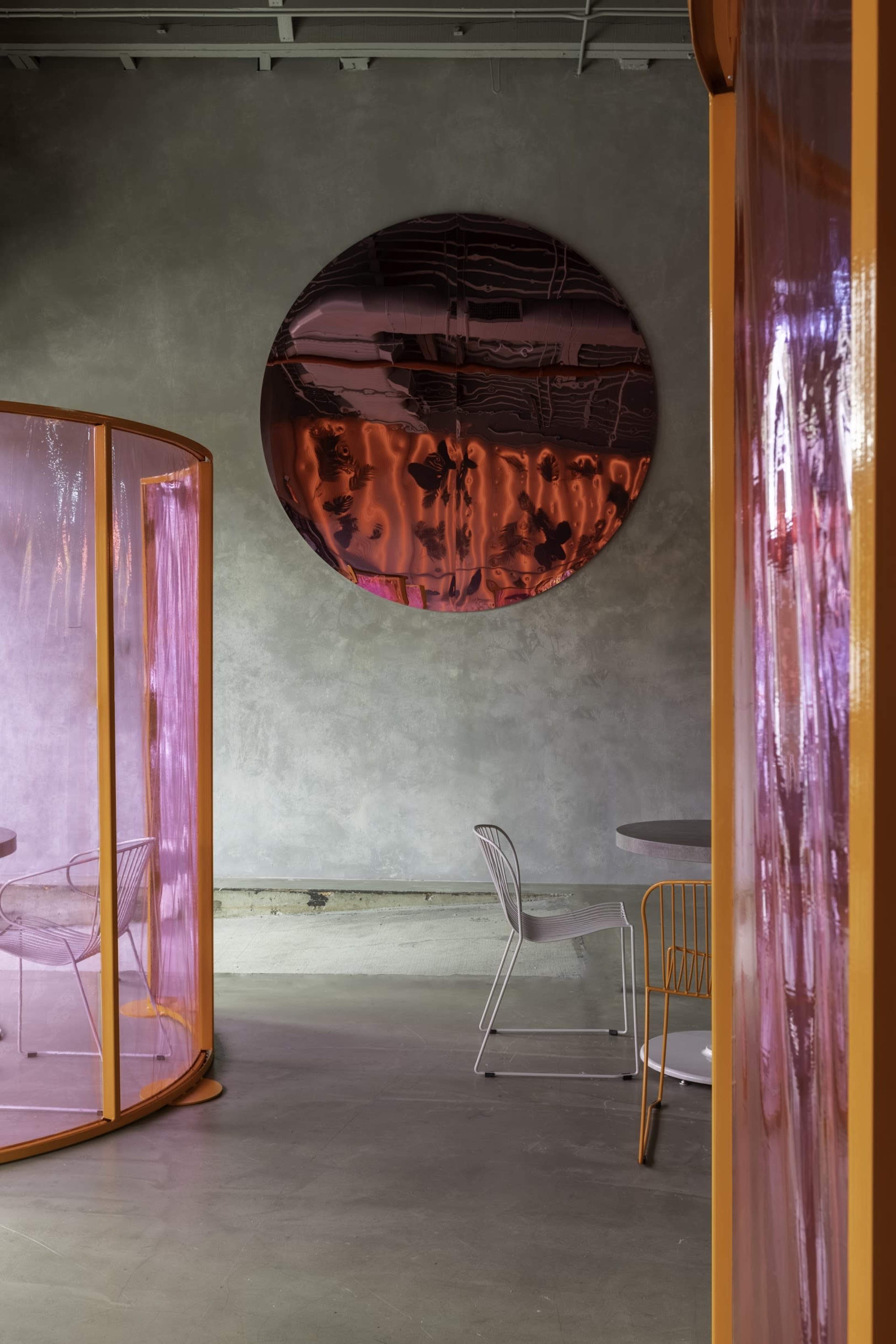 A modern interior space featuring translucent pink partitions, circular reflective artwork on the wall, and minimalist furniture.