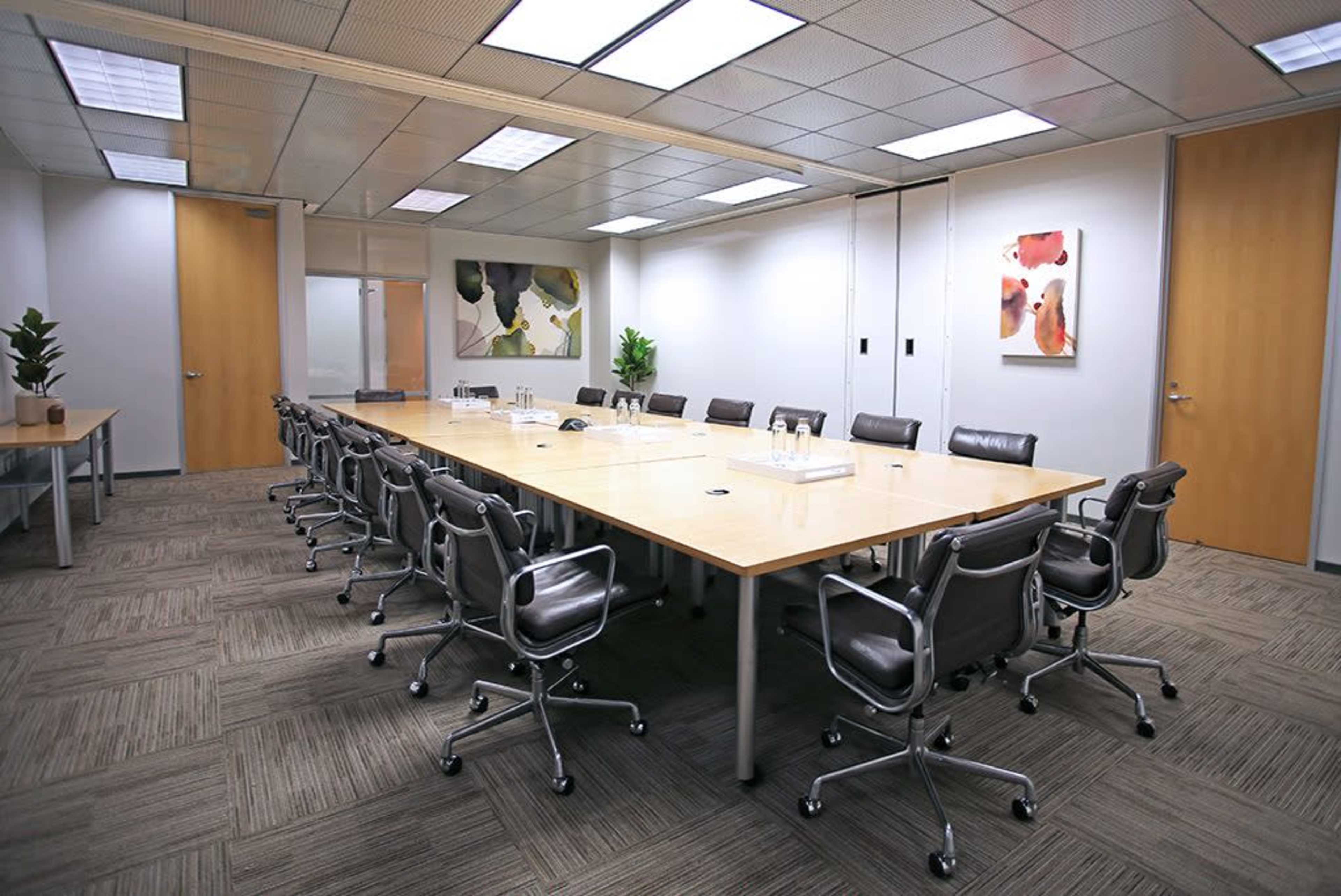 A large conference room features a long wooden table surrounded by several chairs, with artwork and plants enhancing the space.