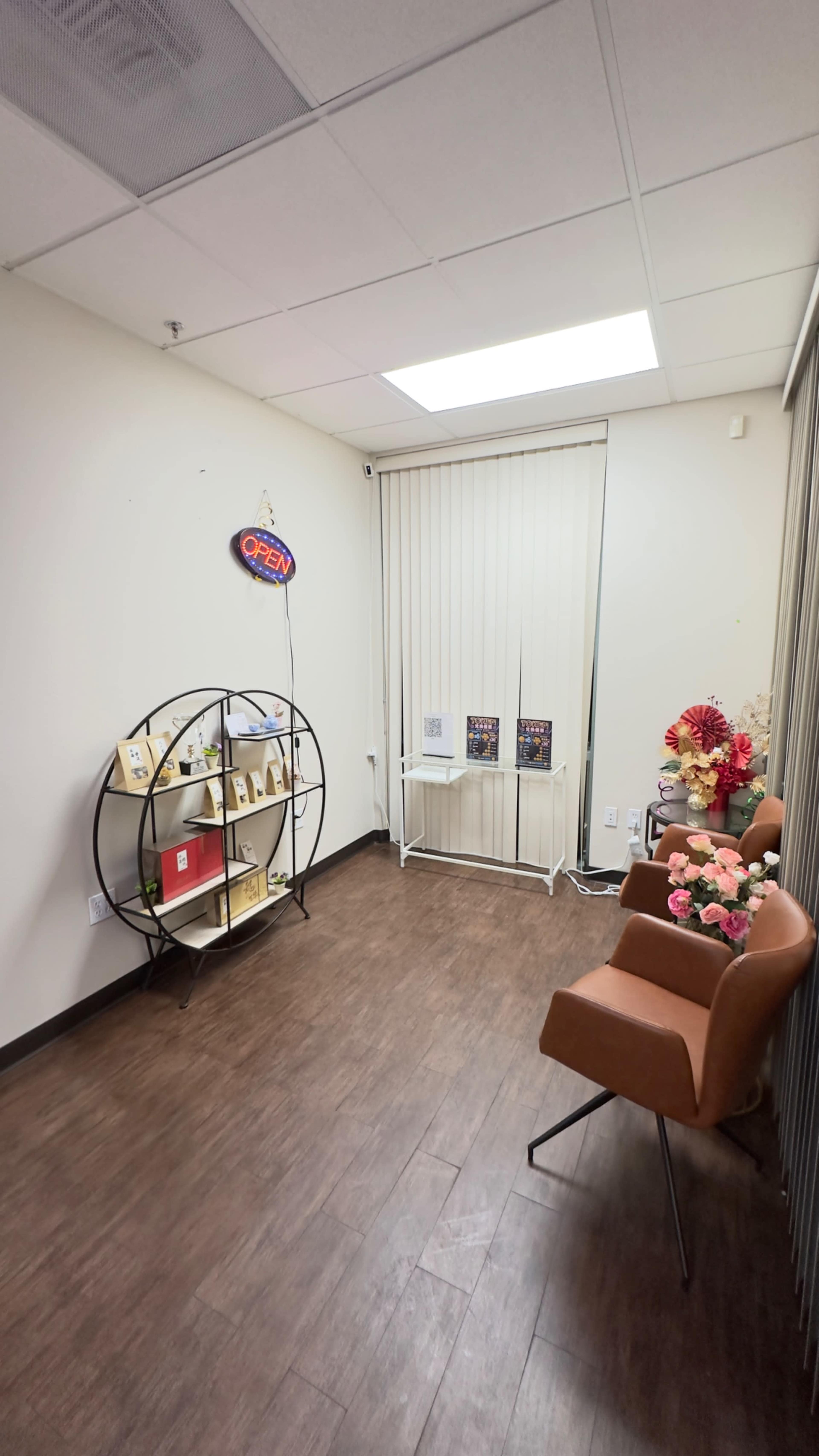 The image shows a small room with a circular shelf displaying items, a brown armchair, and a decorative arrangement of flowers.