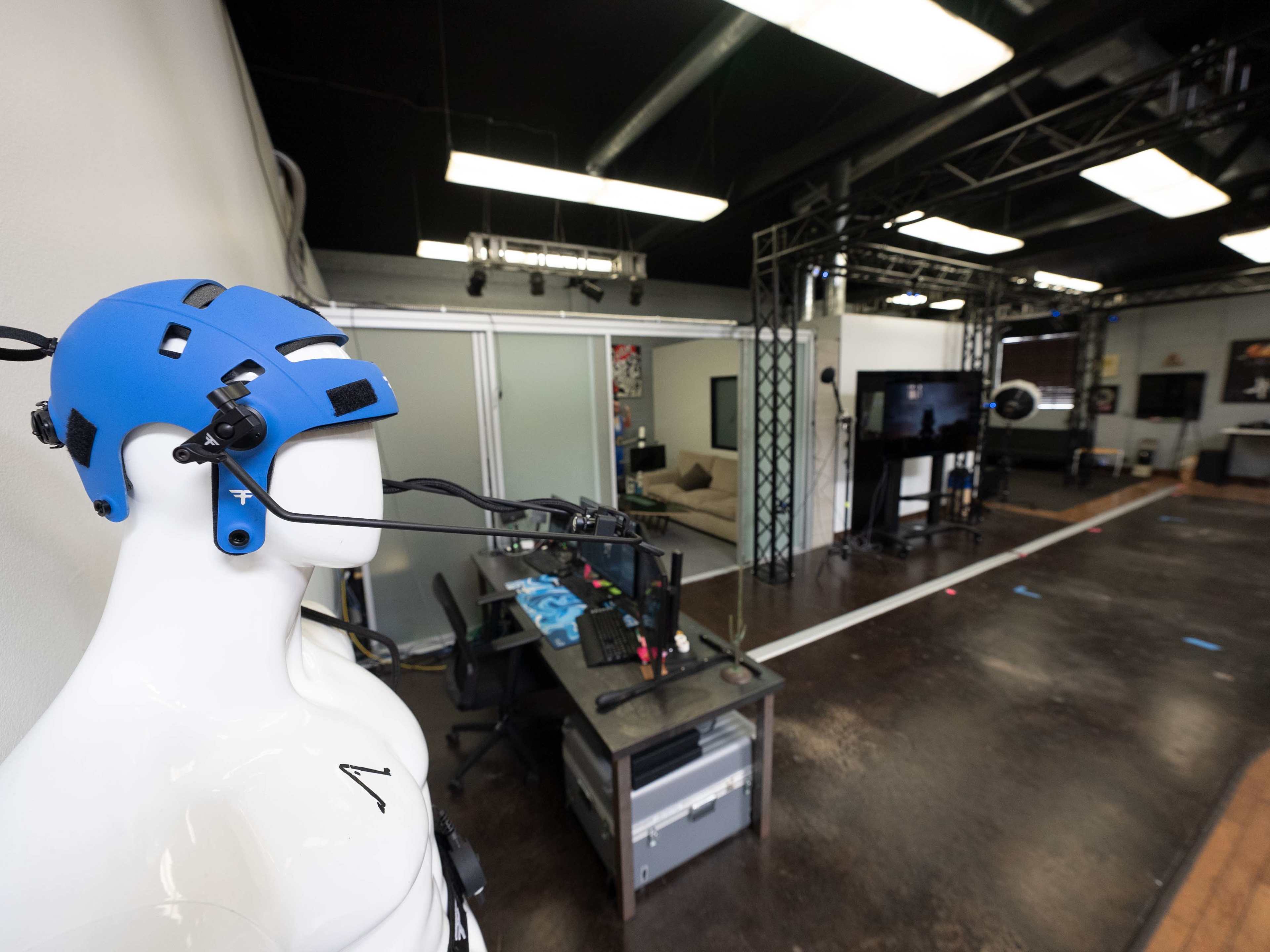 A blue helmet is mounted on a mannequin in an indoor studio equipped with various technology and equipment.