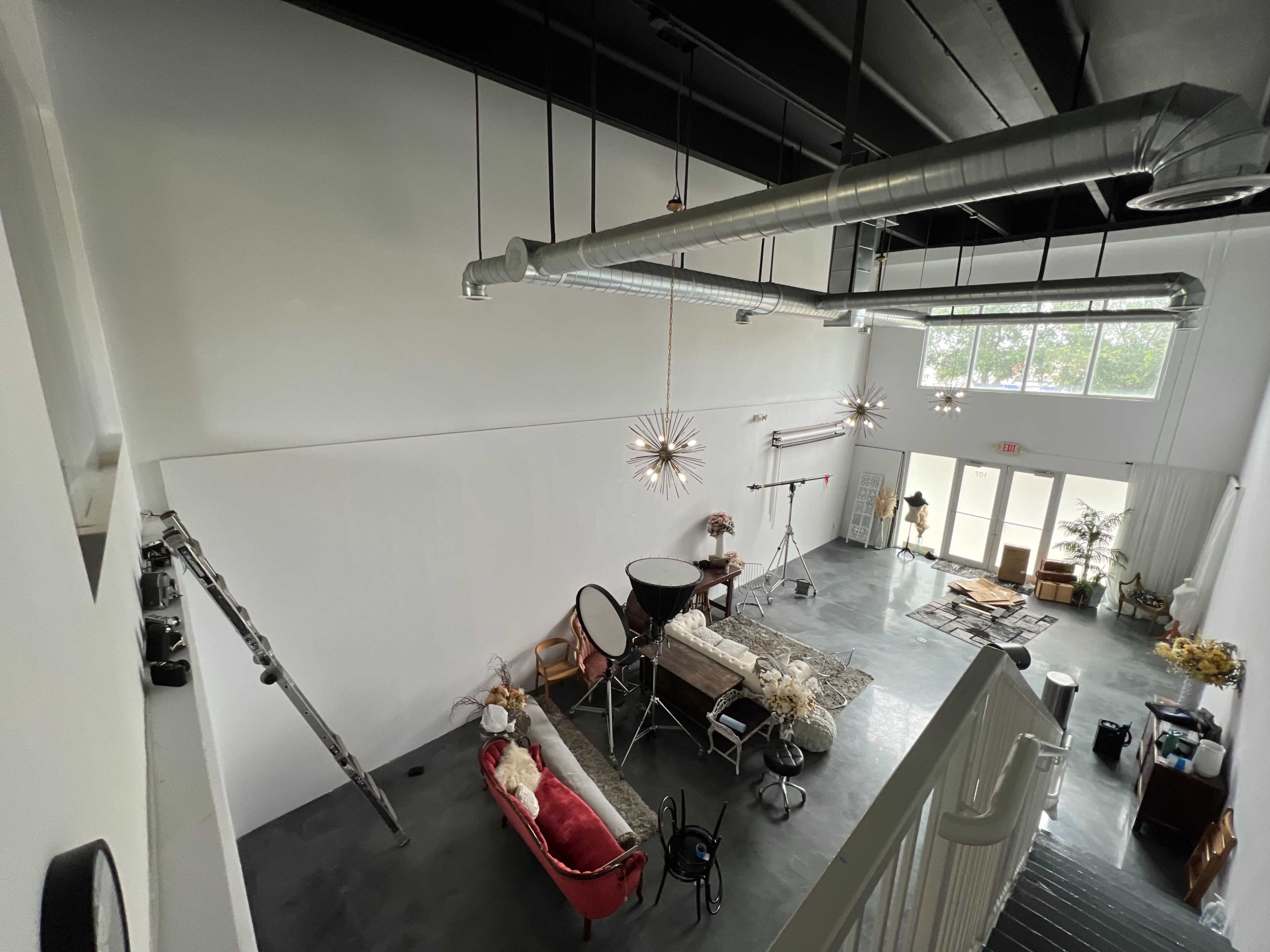 A spacious, well-lit studio with high ceilings, featuring a red sofa, a decoratively set table, and various photography equipment.