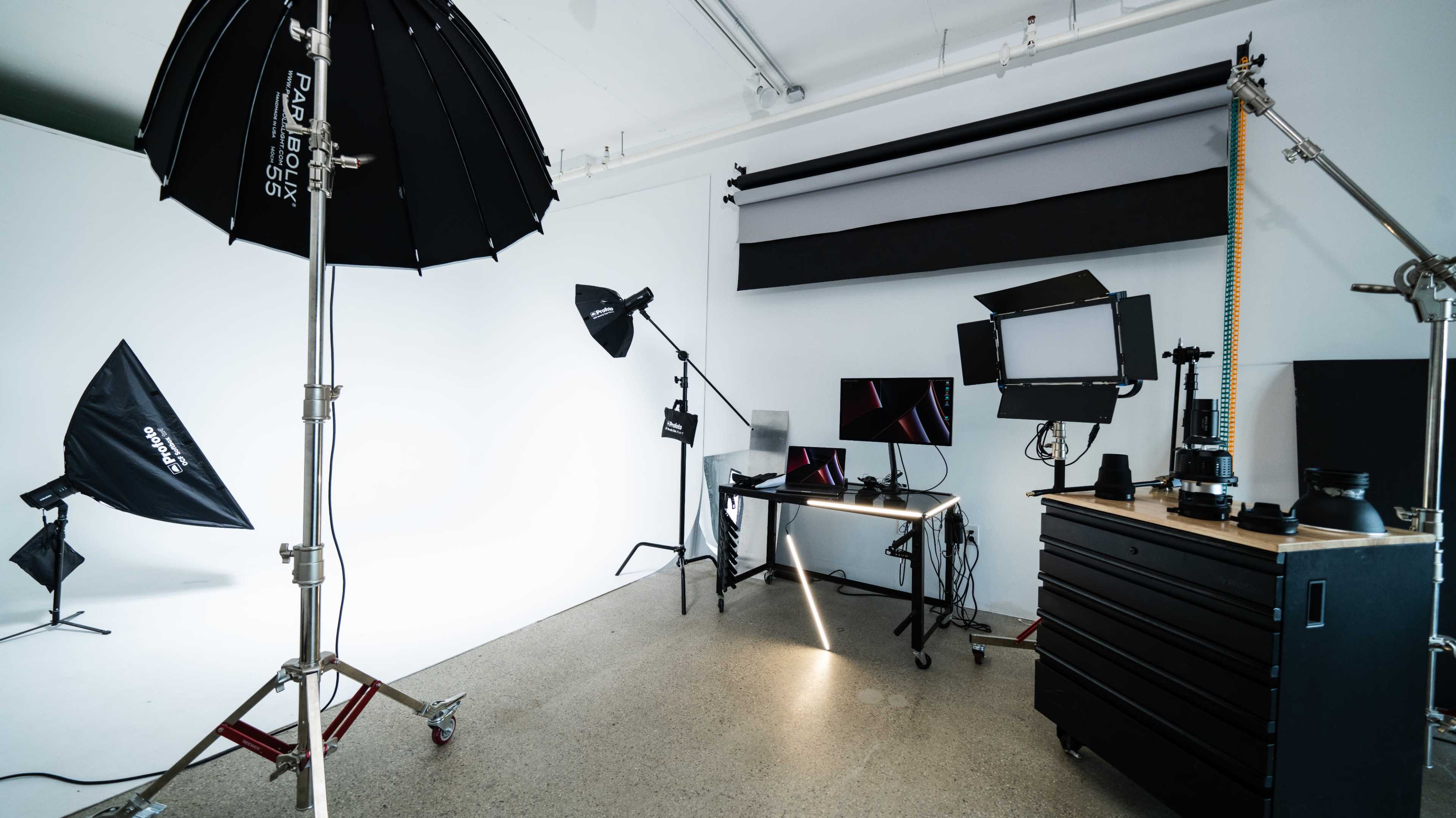 A photography studio equipped with various lighting setups, a computer workstation, and a storage cart.