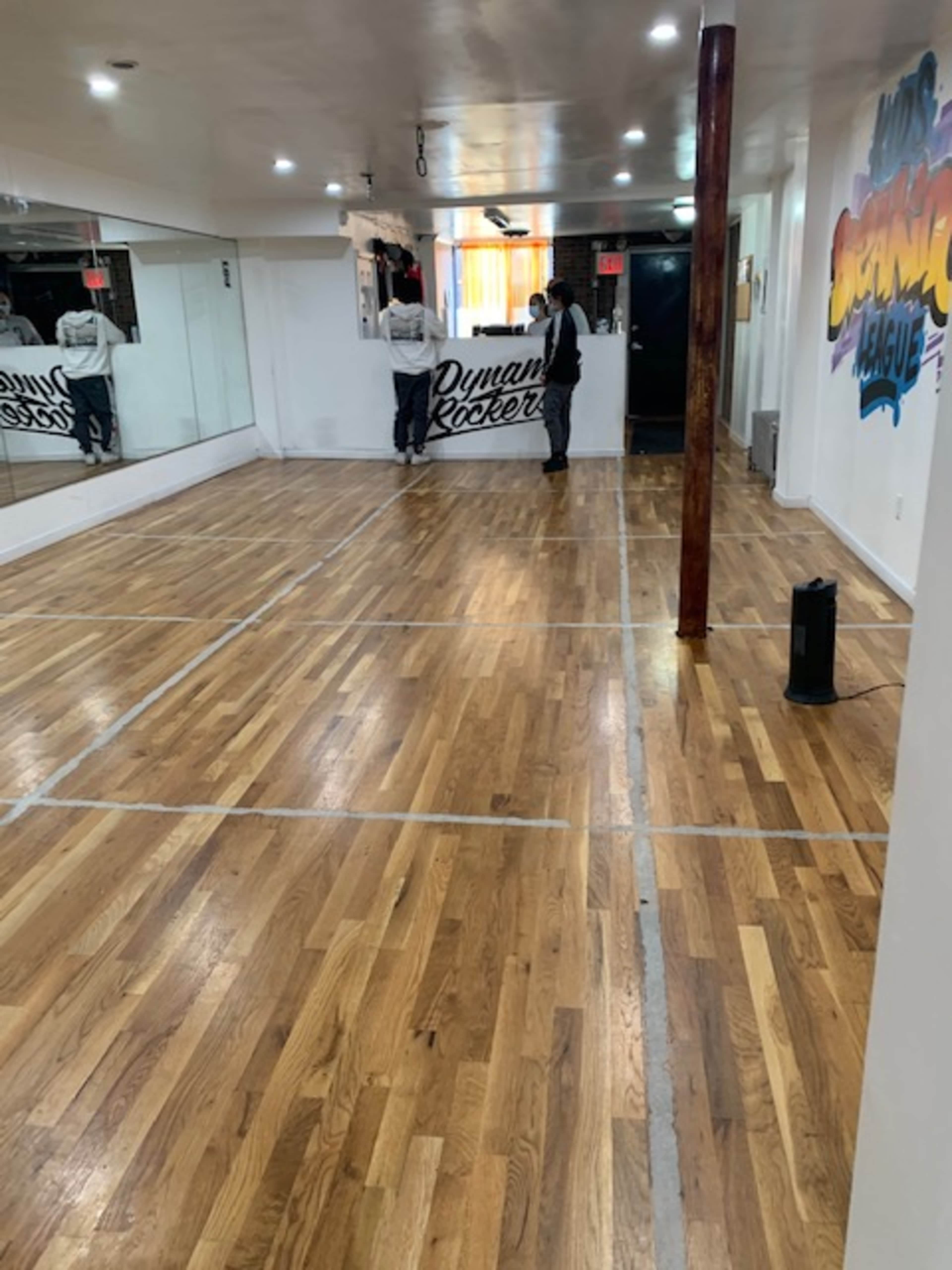 A spacious wooden-floored studio features a mirrored wall and a sign for "Dynamic Rockers" in the background.