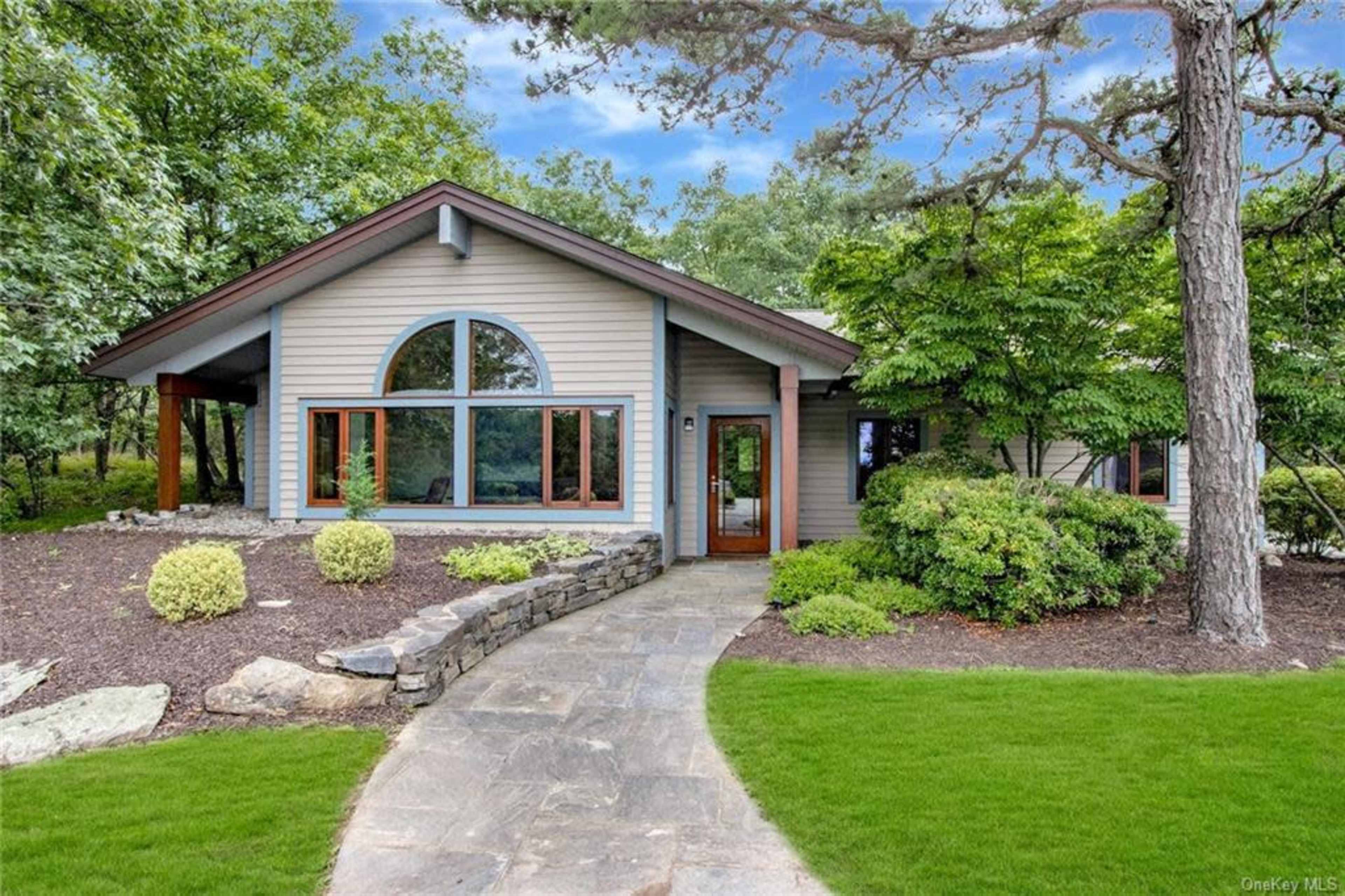 A modern single-story house is surrounded by landscaped gardens and a stone walkway.