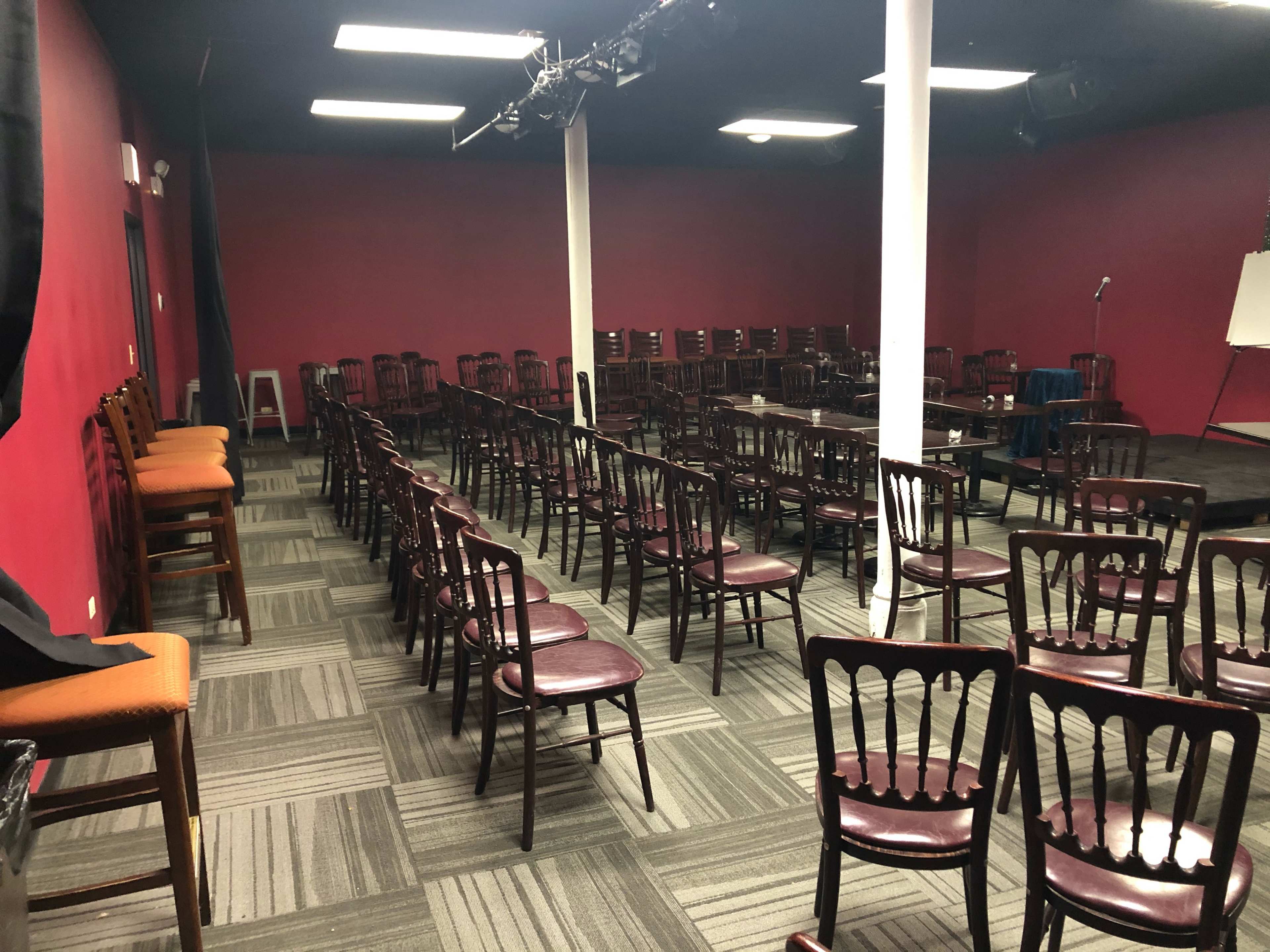 A performance space with rows of wooden chairs facing a small stage area in a room with red walls.
