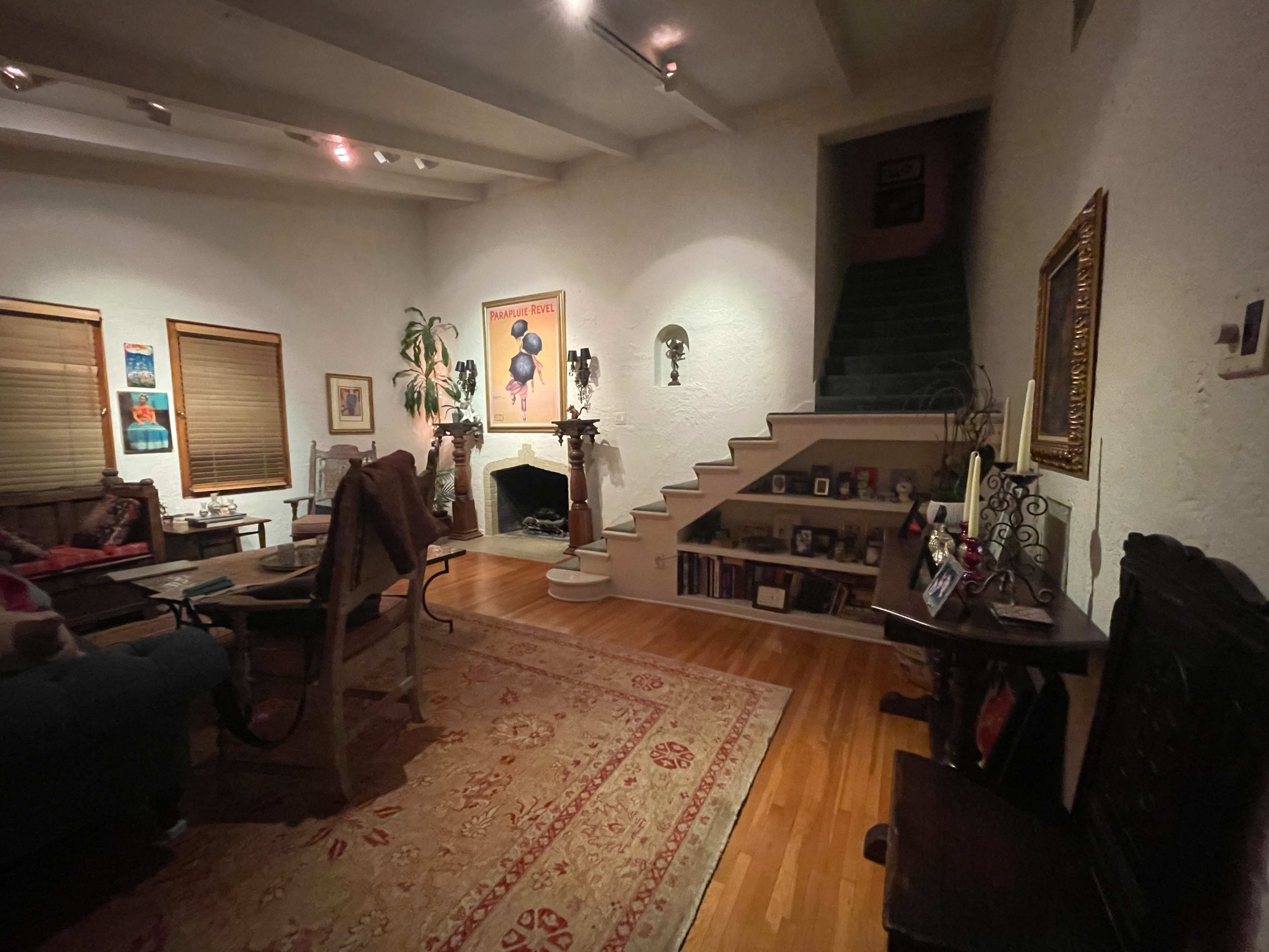 A cozy living room with a staircase leading to an upper level, a fireplace, and various decorations on the walls and shelves.
