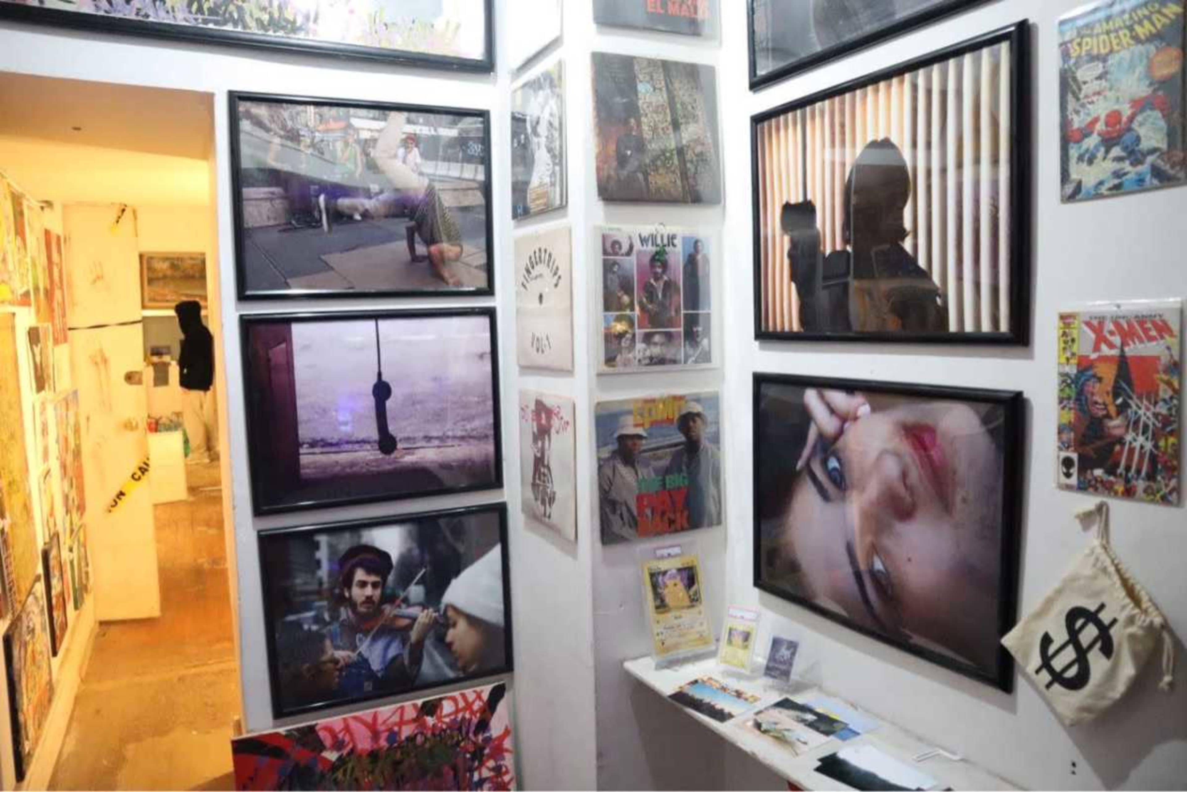 The image shows a narrow hallway adorned with colorful art pieces, including framed photographs and comic book covers, creating a vibrant display along the walls.