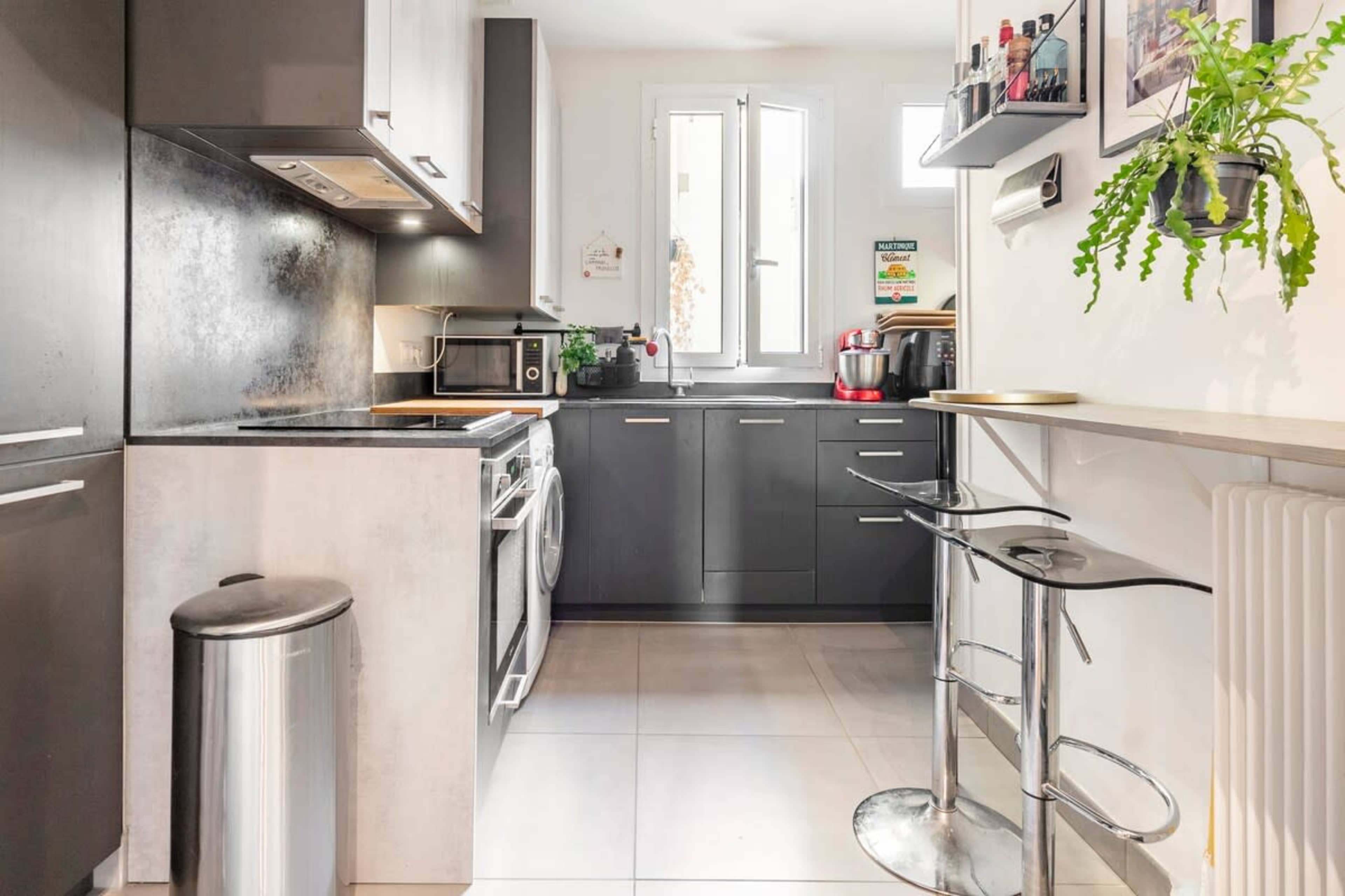 A modern kitchen with stainless steel appliances, dark cabinetry, and a small dining area featuring a bar table and stools.