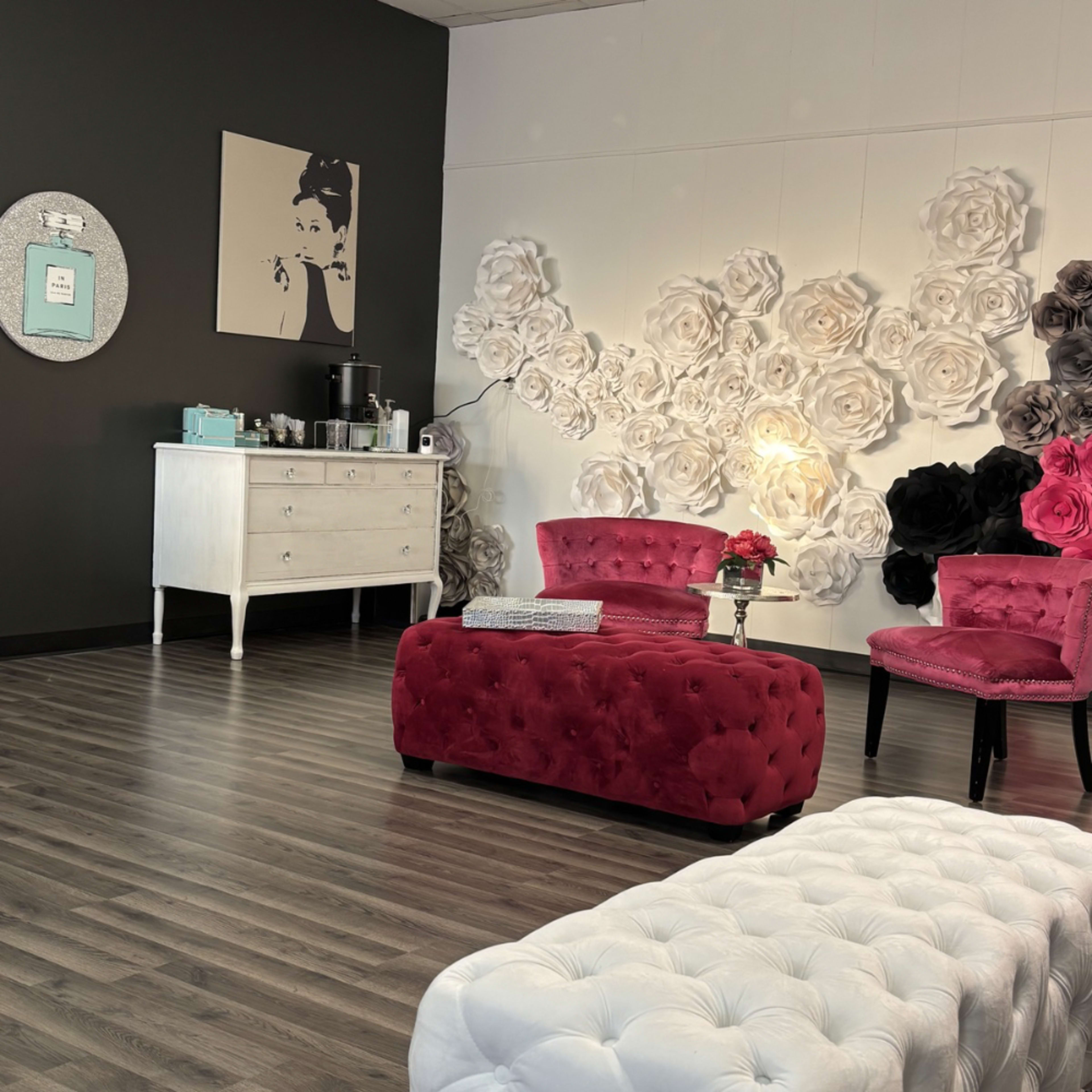 The image shows a modern interior space featuring a white cabinet, pink tufted chairs, and a wall adorned with large paper flowers.