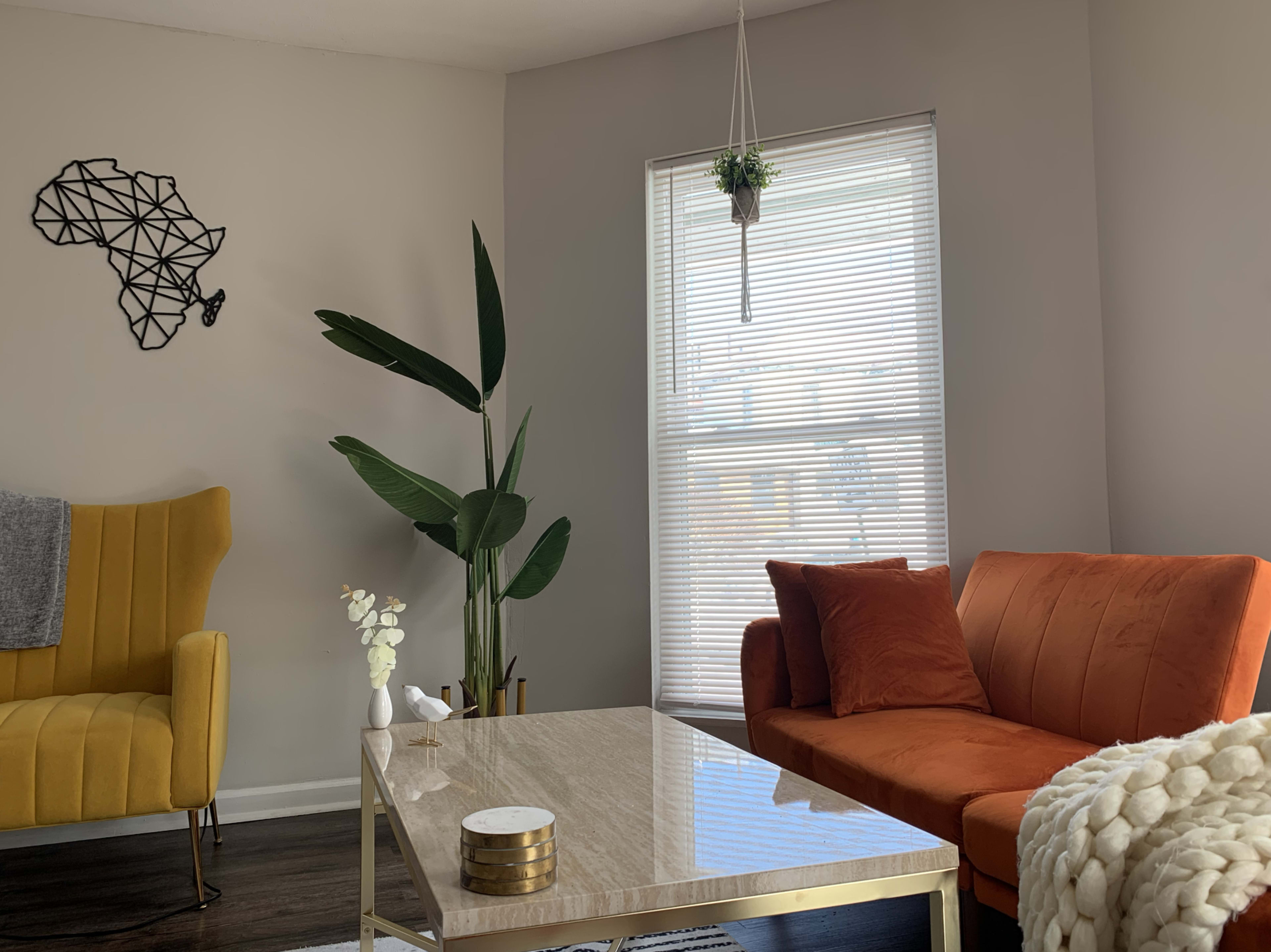 A modern living room with an orange sofa, a yellow accent chair, a coffee table, and a wall decoration of the African continent.