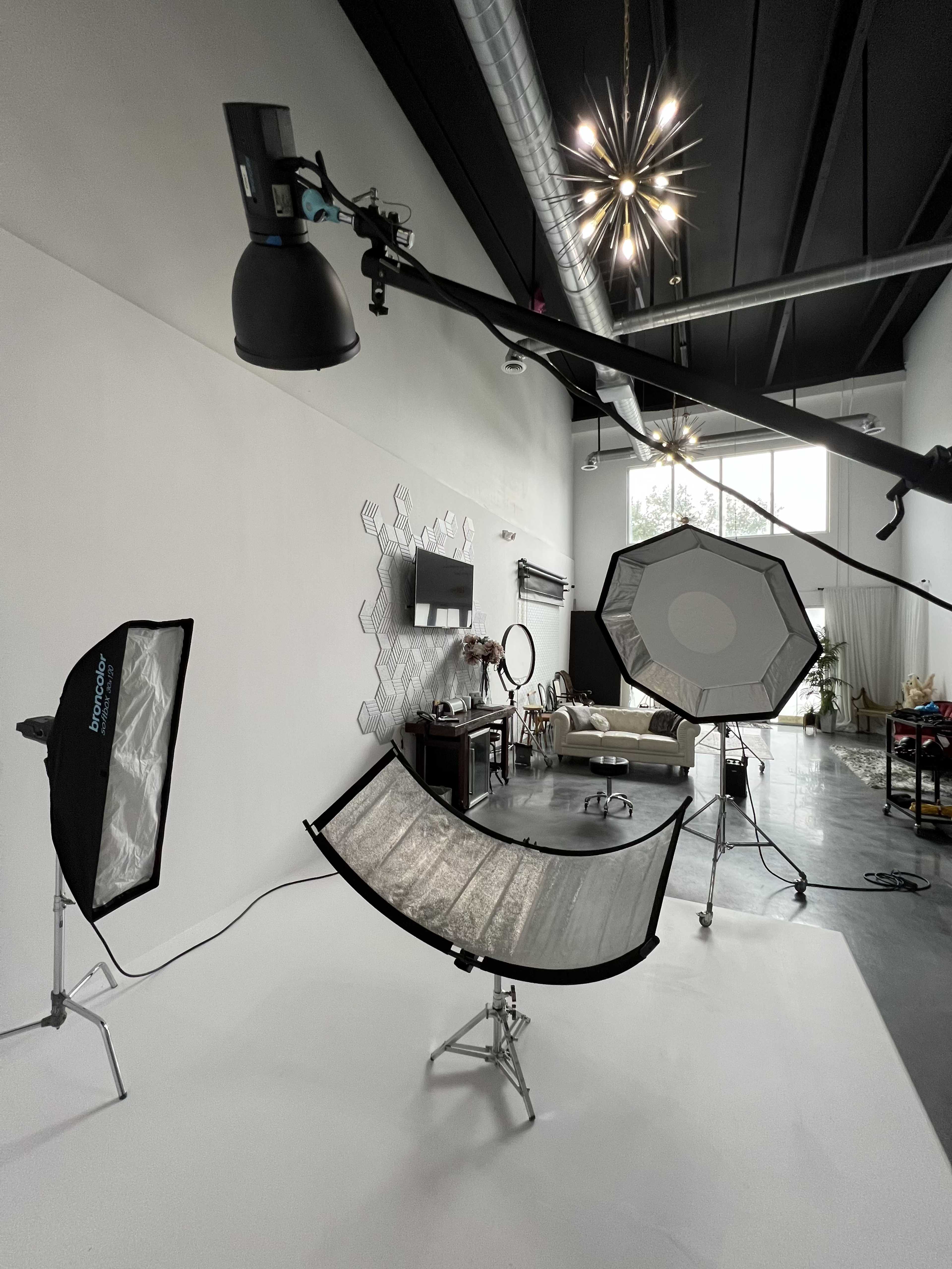 A photography studio is set up with multiple lighting equipment, reflectors, and a backdrop, all ready for a shoot.
