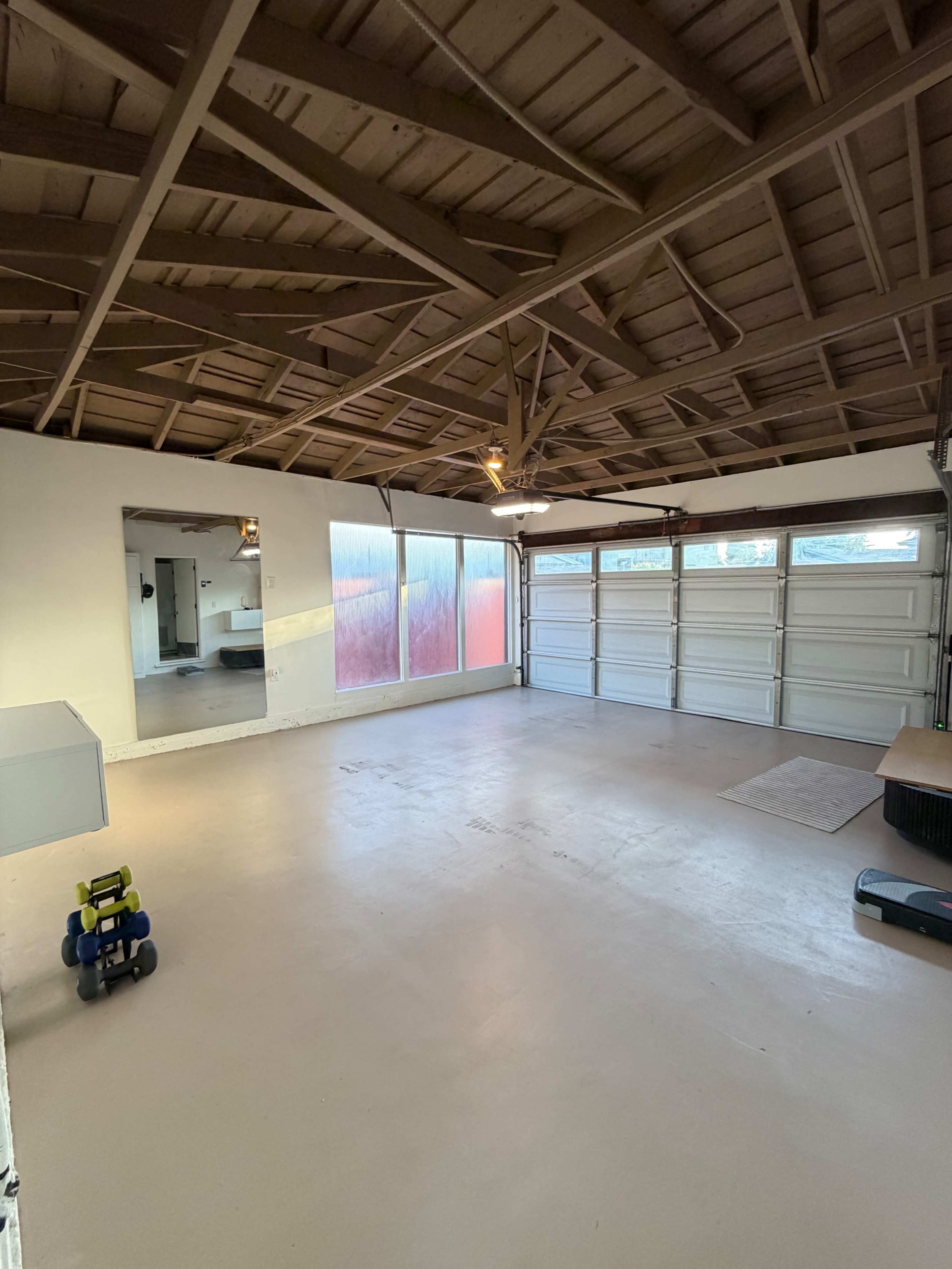 The image shows an empty garage with exposed wooden beams, a concrete floor, and large garage doors on one side.