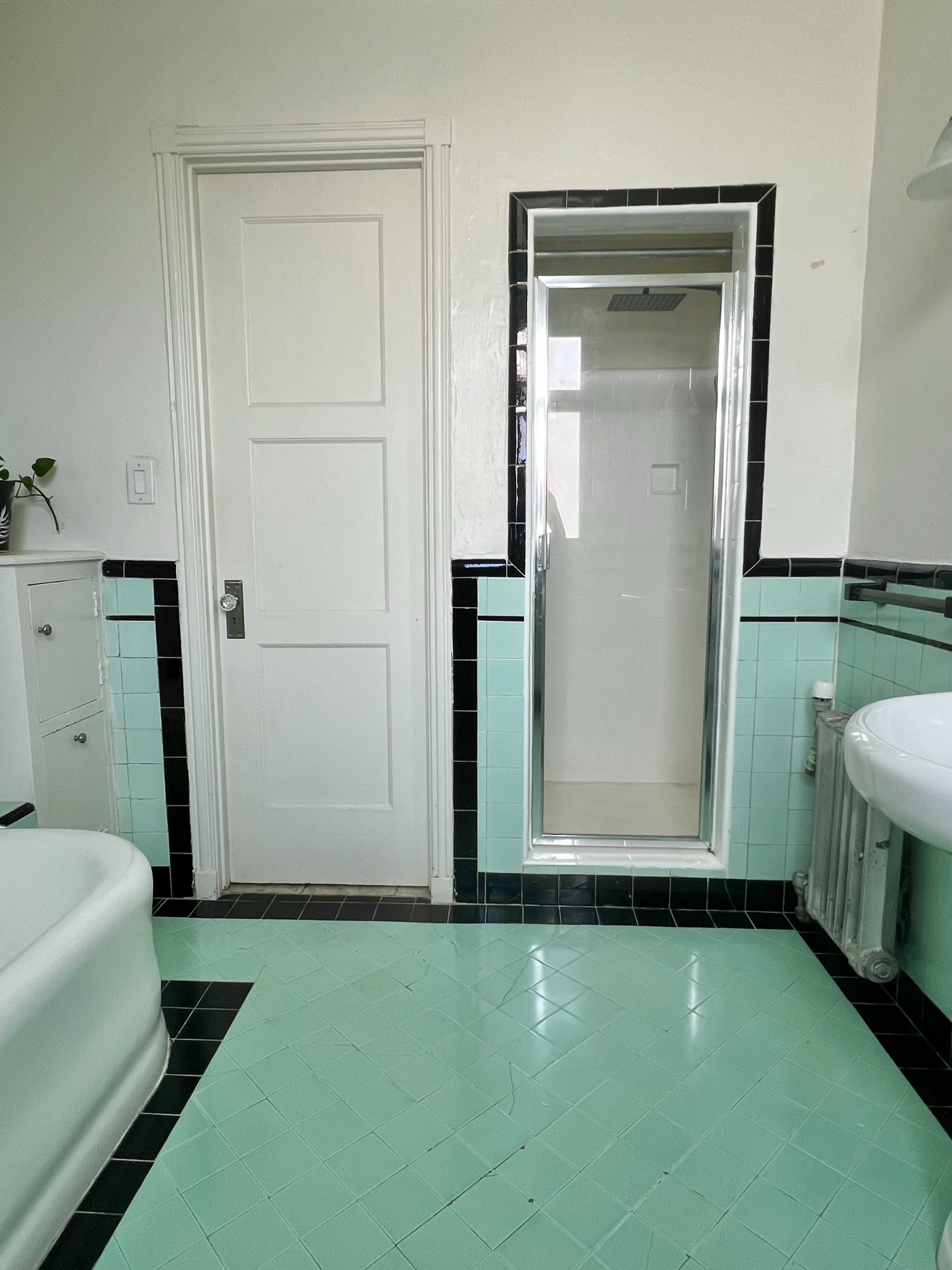 The image shows a bathroom featuring mint green and black tile flooring, a white bathtub, a shower stall, and a door leading to another room.