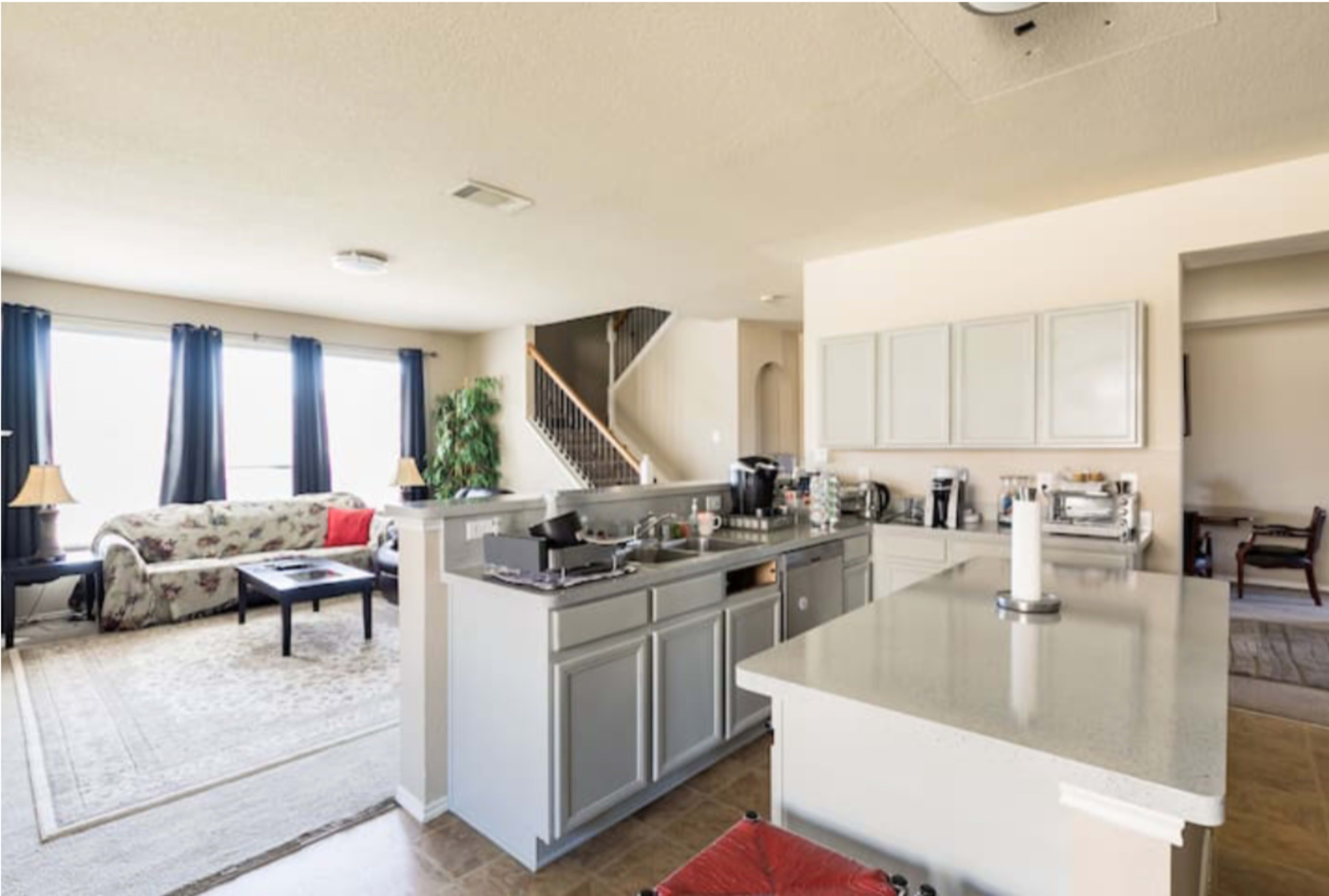 An open-concept kitchen and living area with a staircase in the background and a sofa facing a coffee table.