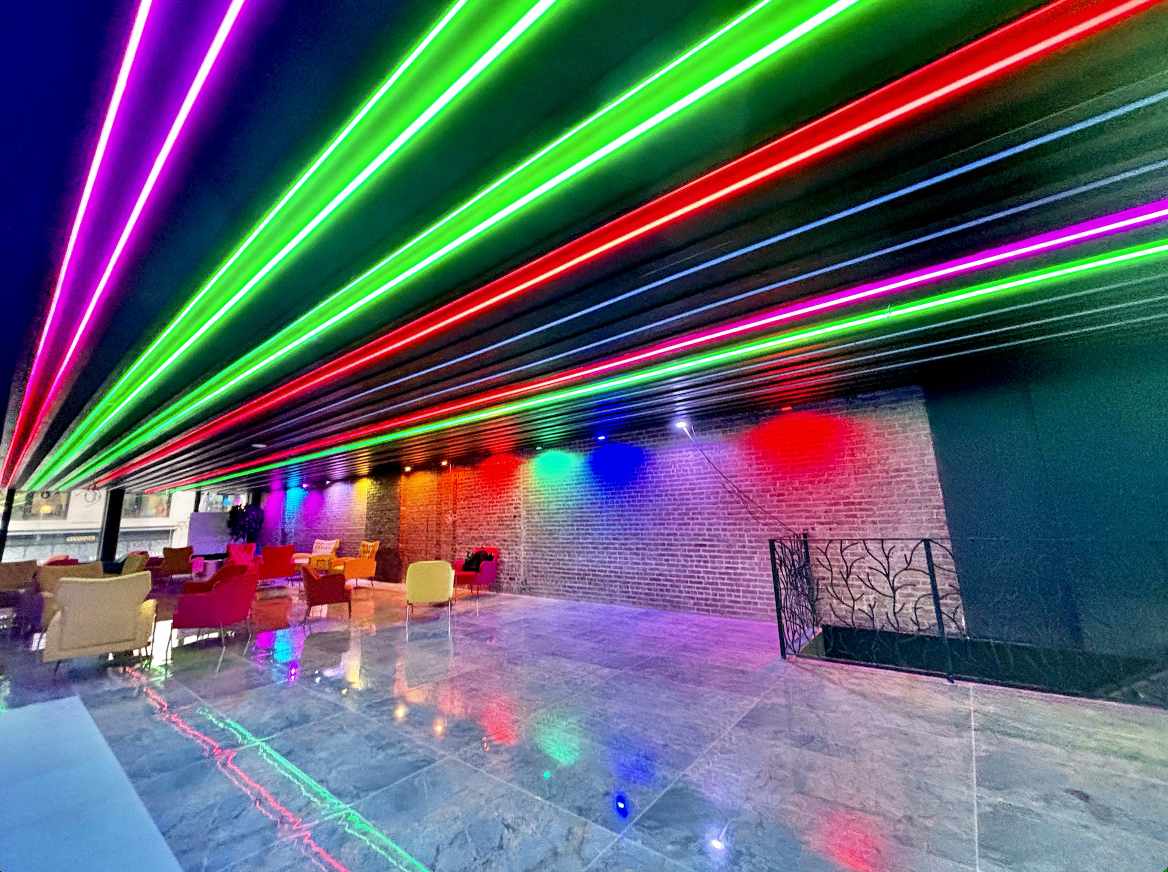 A modern interior space with a glossy floor and colorful neon lights illuminating the ceiling and walls.