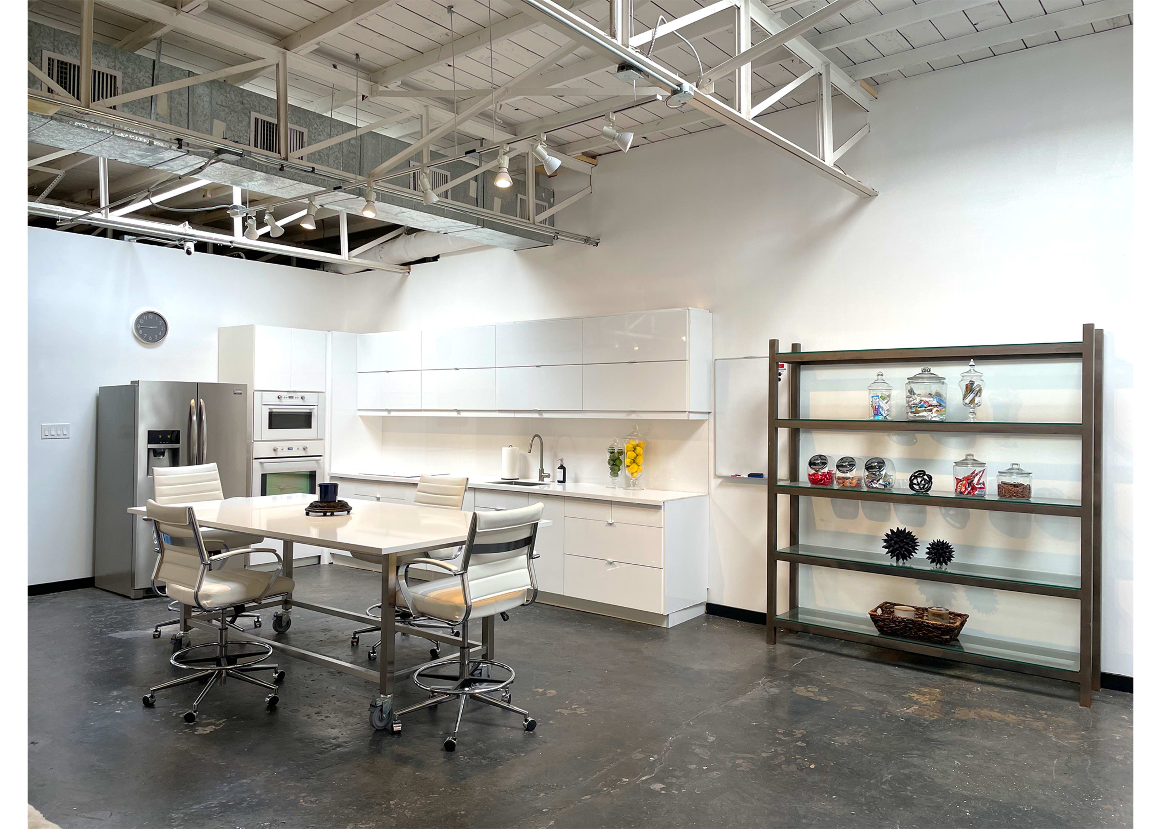 A modern kitchen with white cabinetry, a central island with bar stools, and a glass shelving unit displaying decorative items.