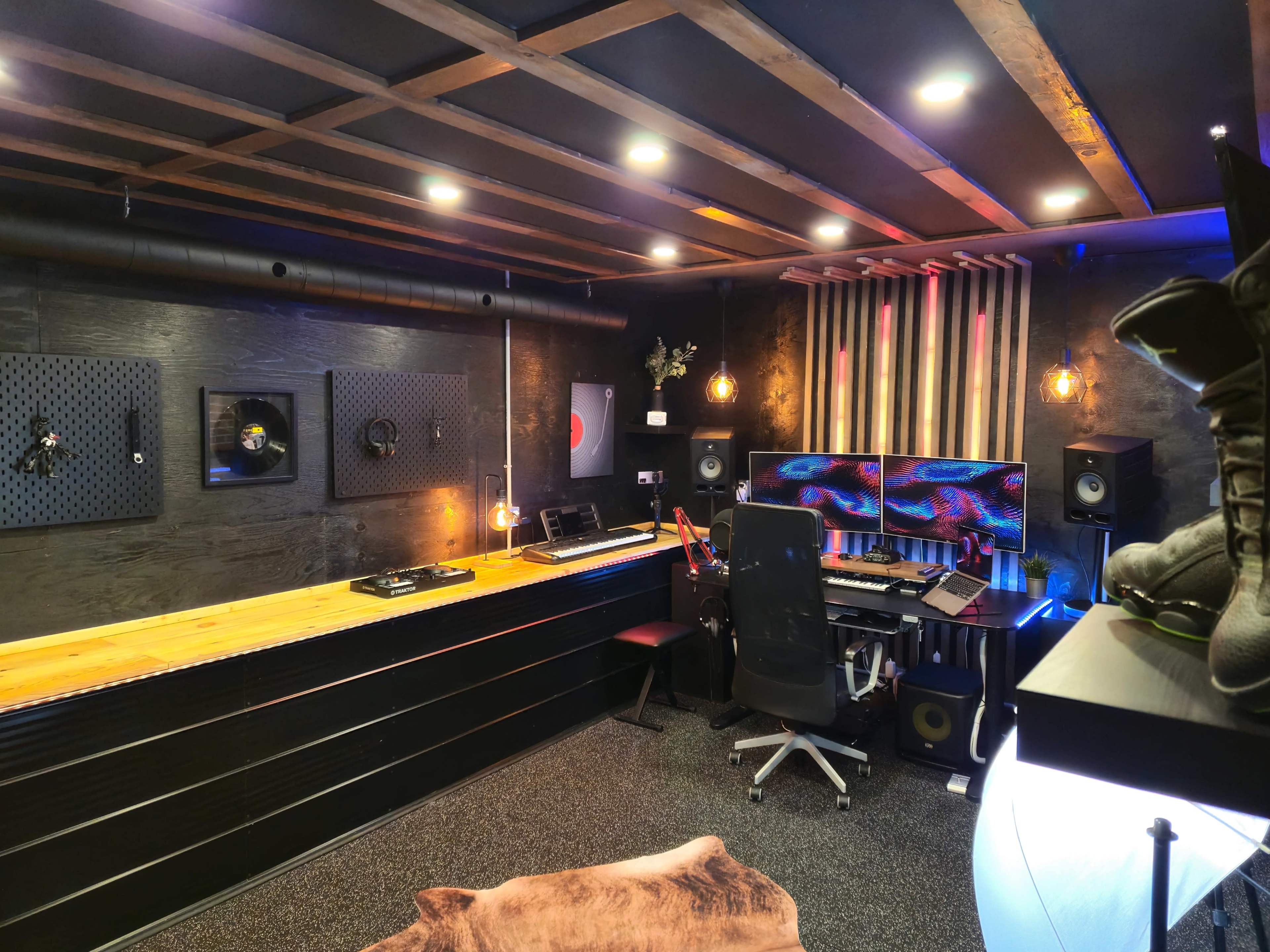 The image shows a modern home studio with dual computer monitors, audio equipment, and a wooden desk under warm lighting.