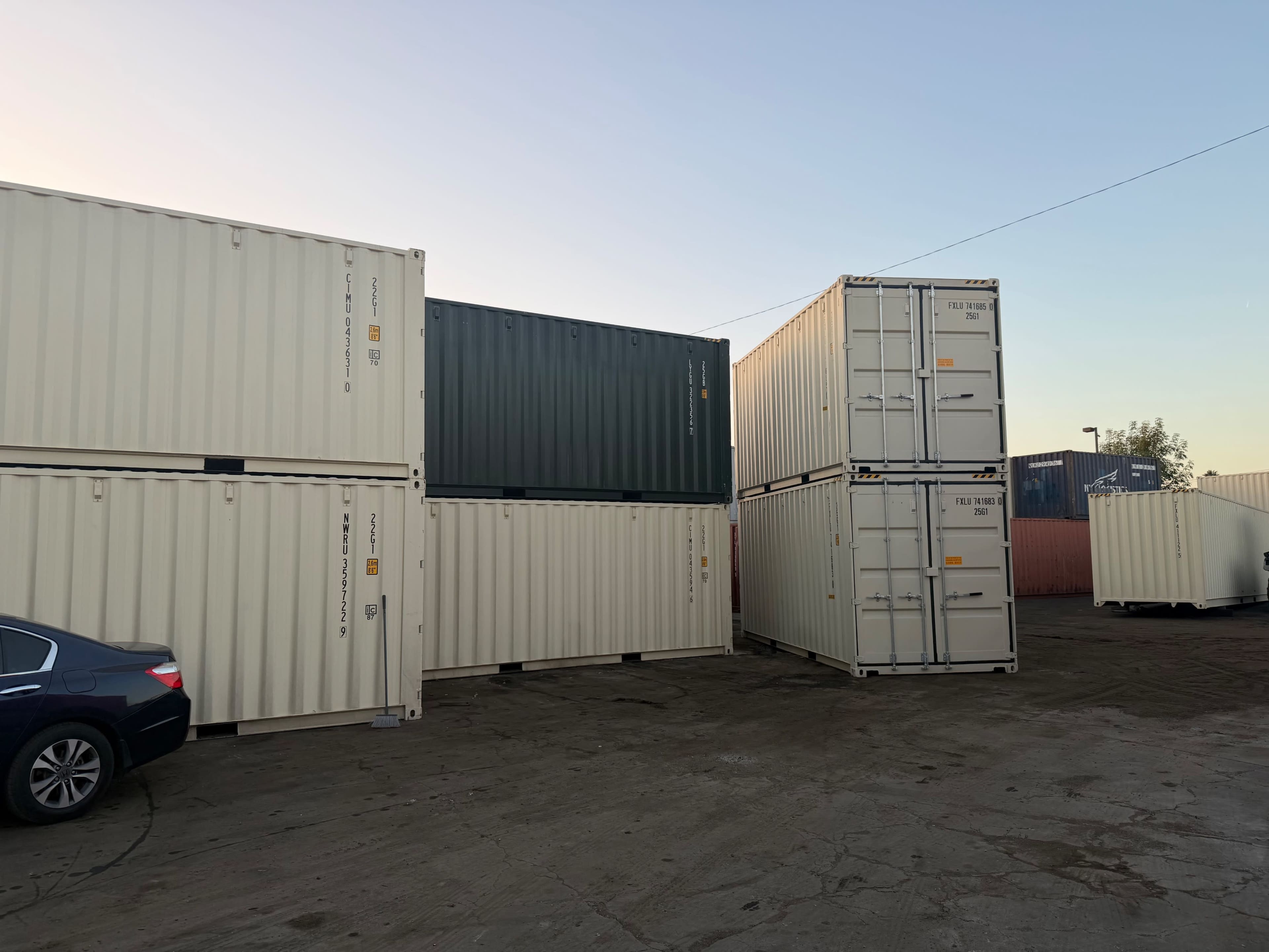 The image shows several shipping containers stacked in a storage yard, with a car parked nearby.
