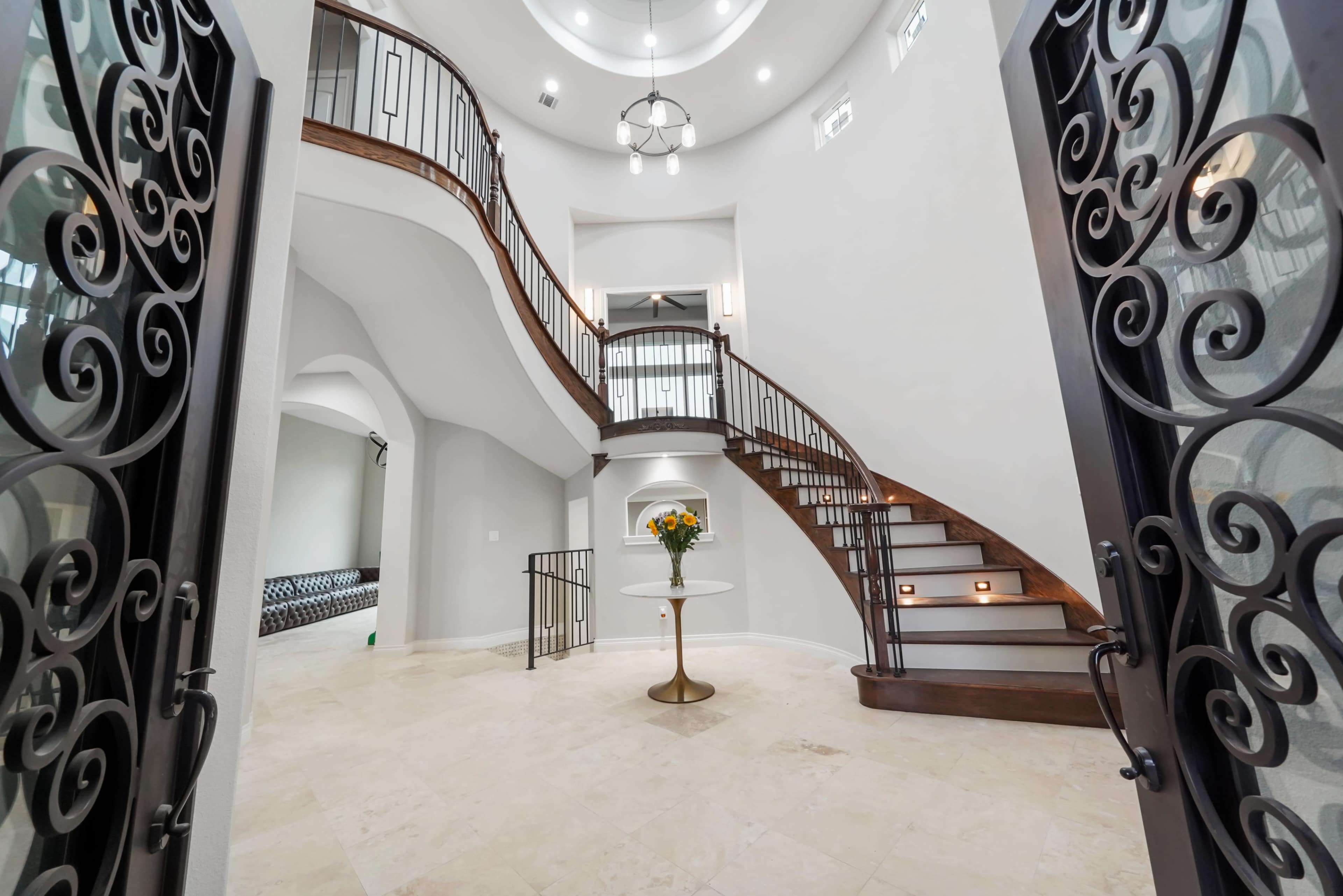 A grand entrance with a spiral staircase, white walls, and decorative metal railings, complemented by a small round table with a flower arrangement.