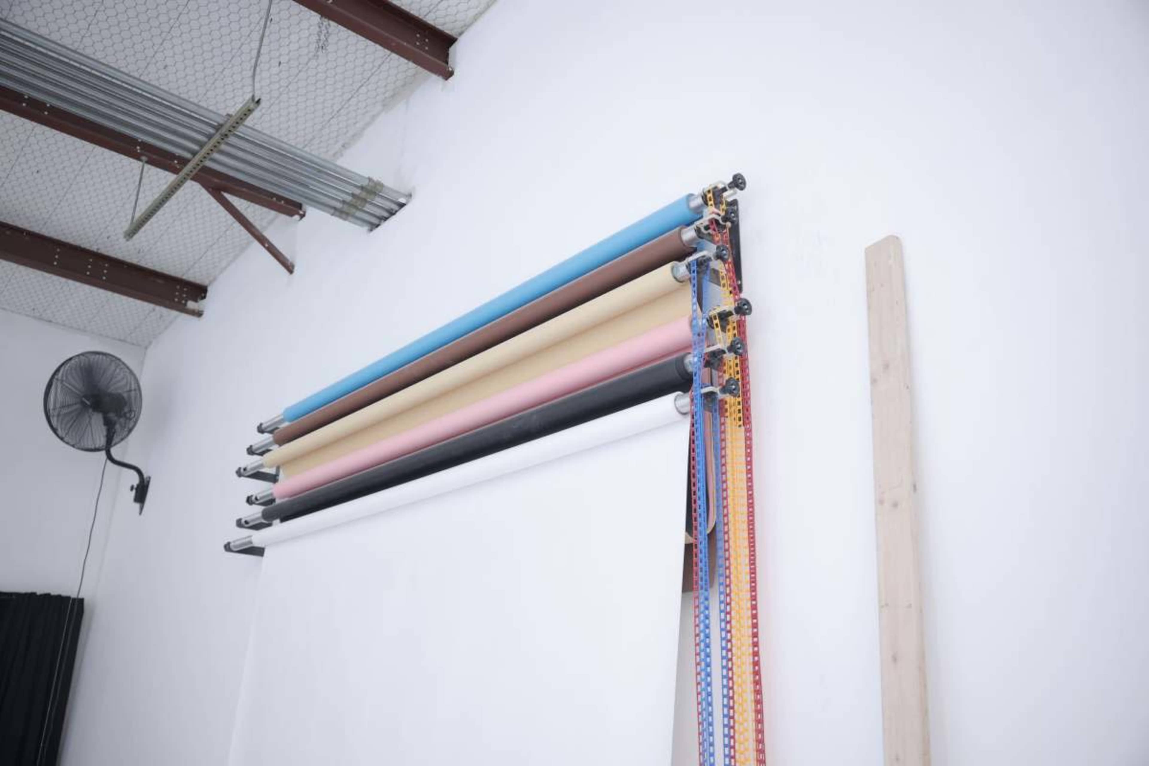 A wall-mounted system holds rolls of colored backdrop paper and hanging cords in a studio setting.