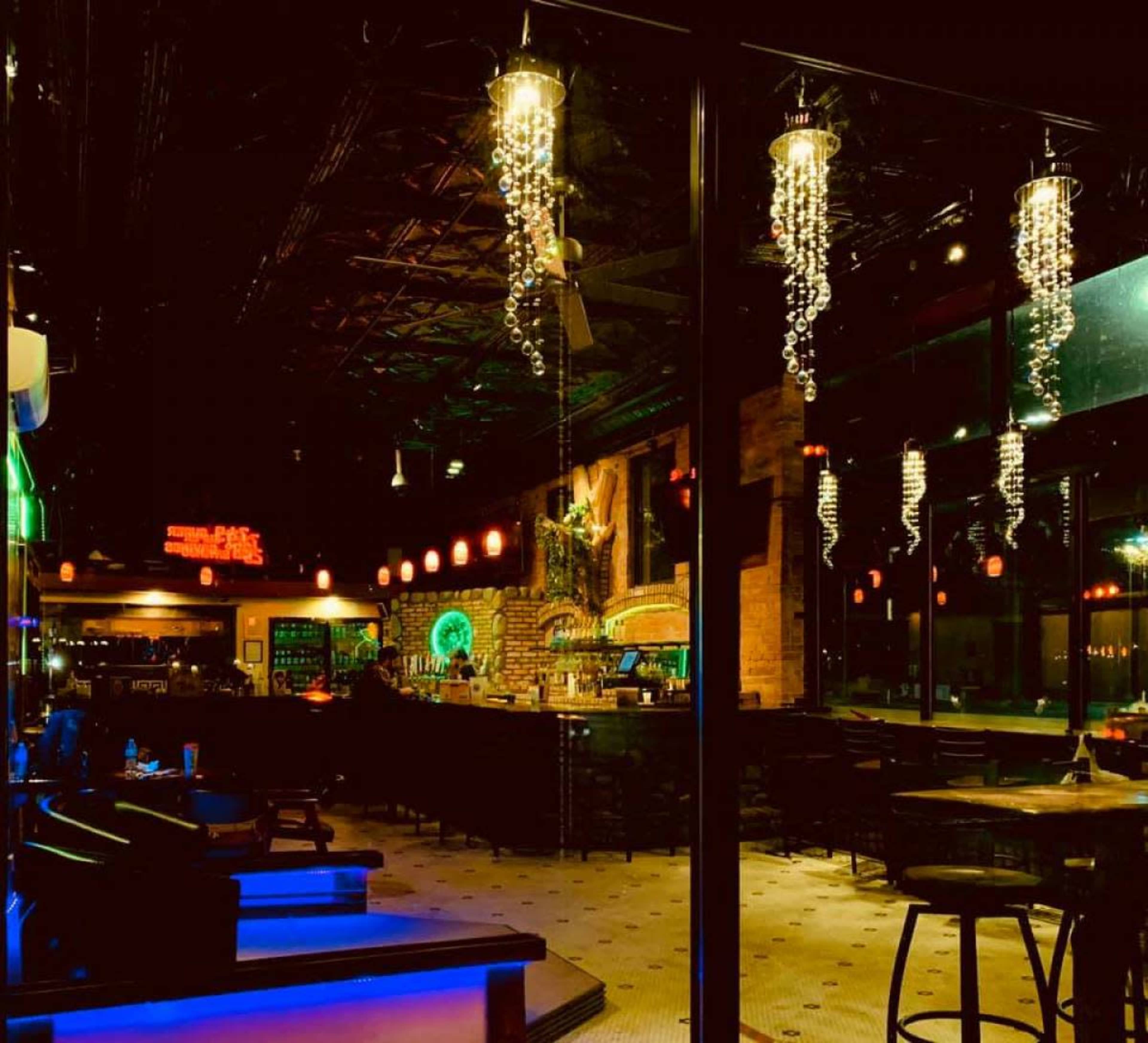 A dimly lit bar with modern decor, featuring hanging light fixtures and a brick wall behind the bar counter.