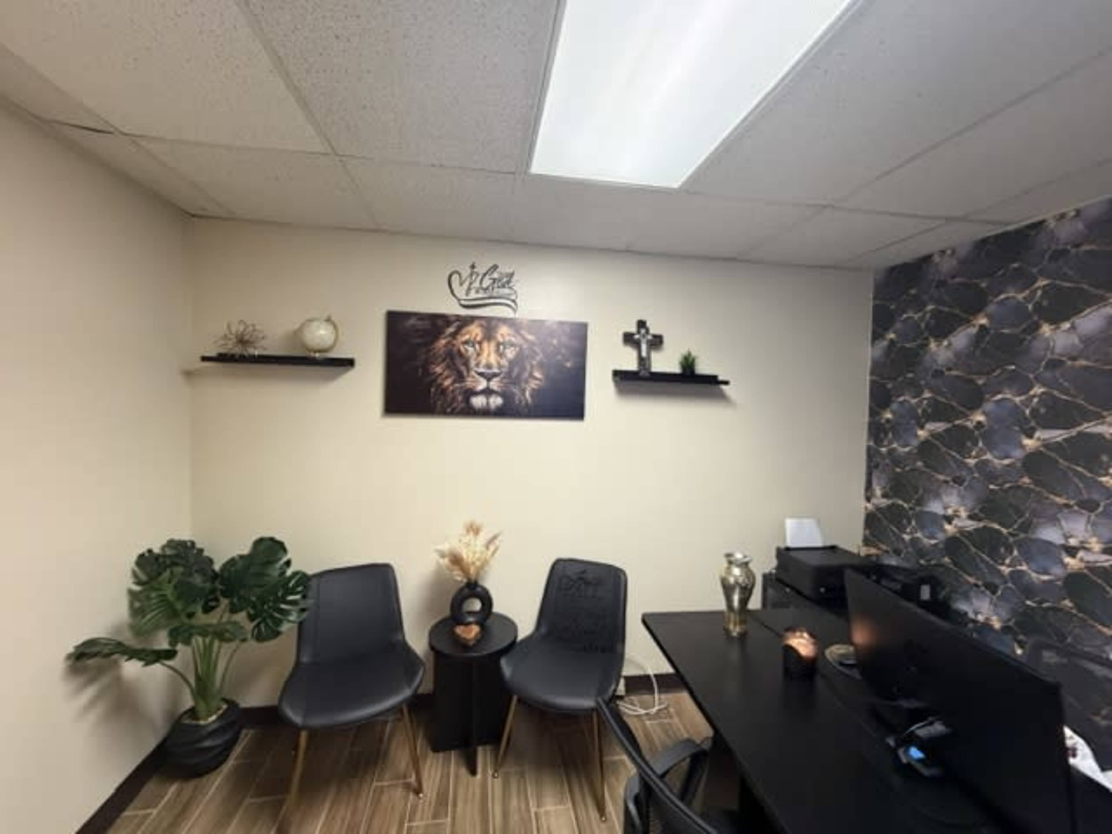 The image shows a small office space with two black chairs, a round table, and a desk, featuring a lion-themed wall art and decorative shelves.