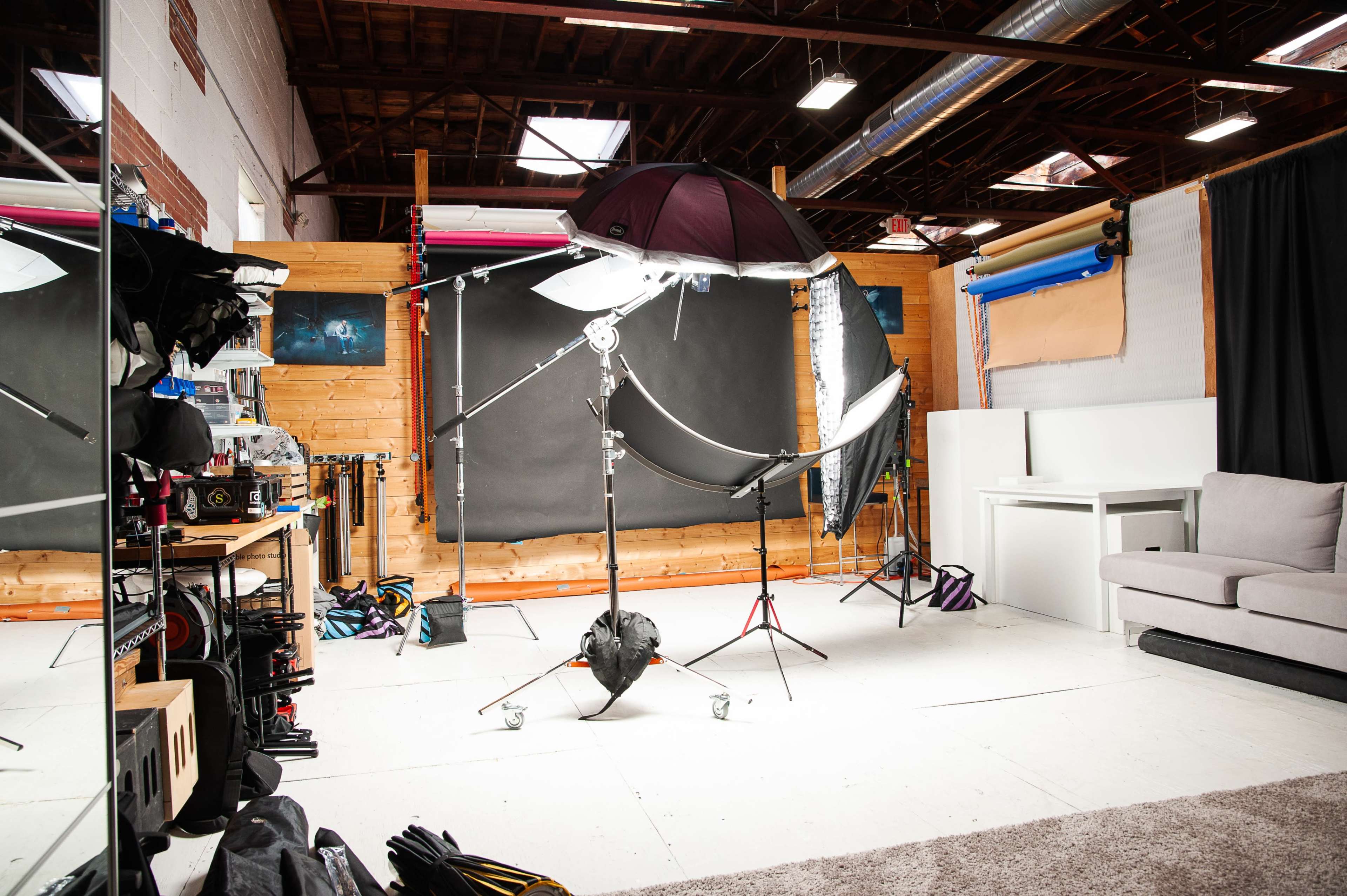 The image shows a photography studio featuring lighting equipment, a black backdrop, and a seating area.