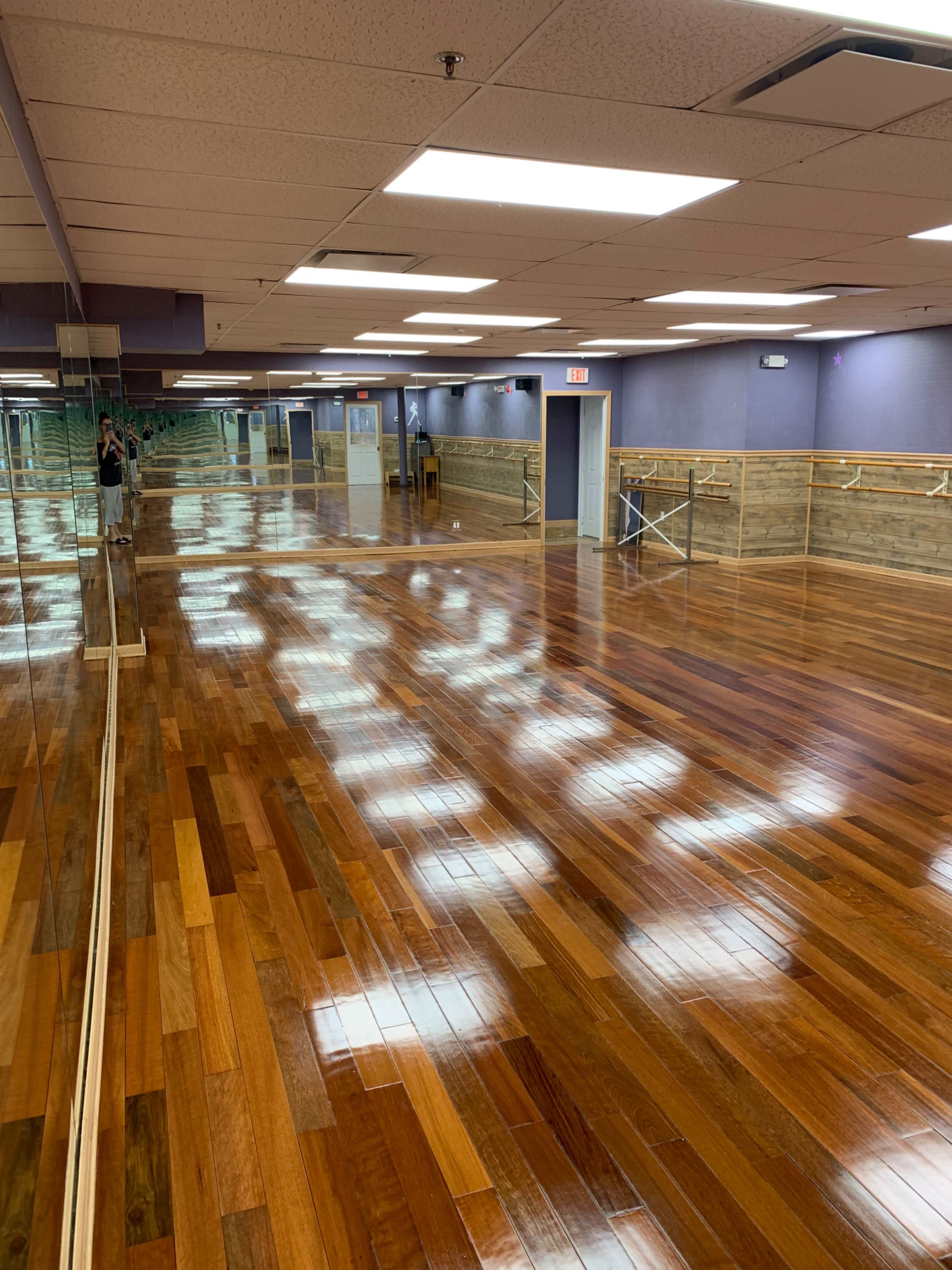 A large dance studio with polished wooden floors and mirrors lining one wall.