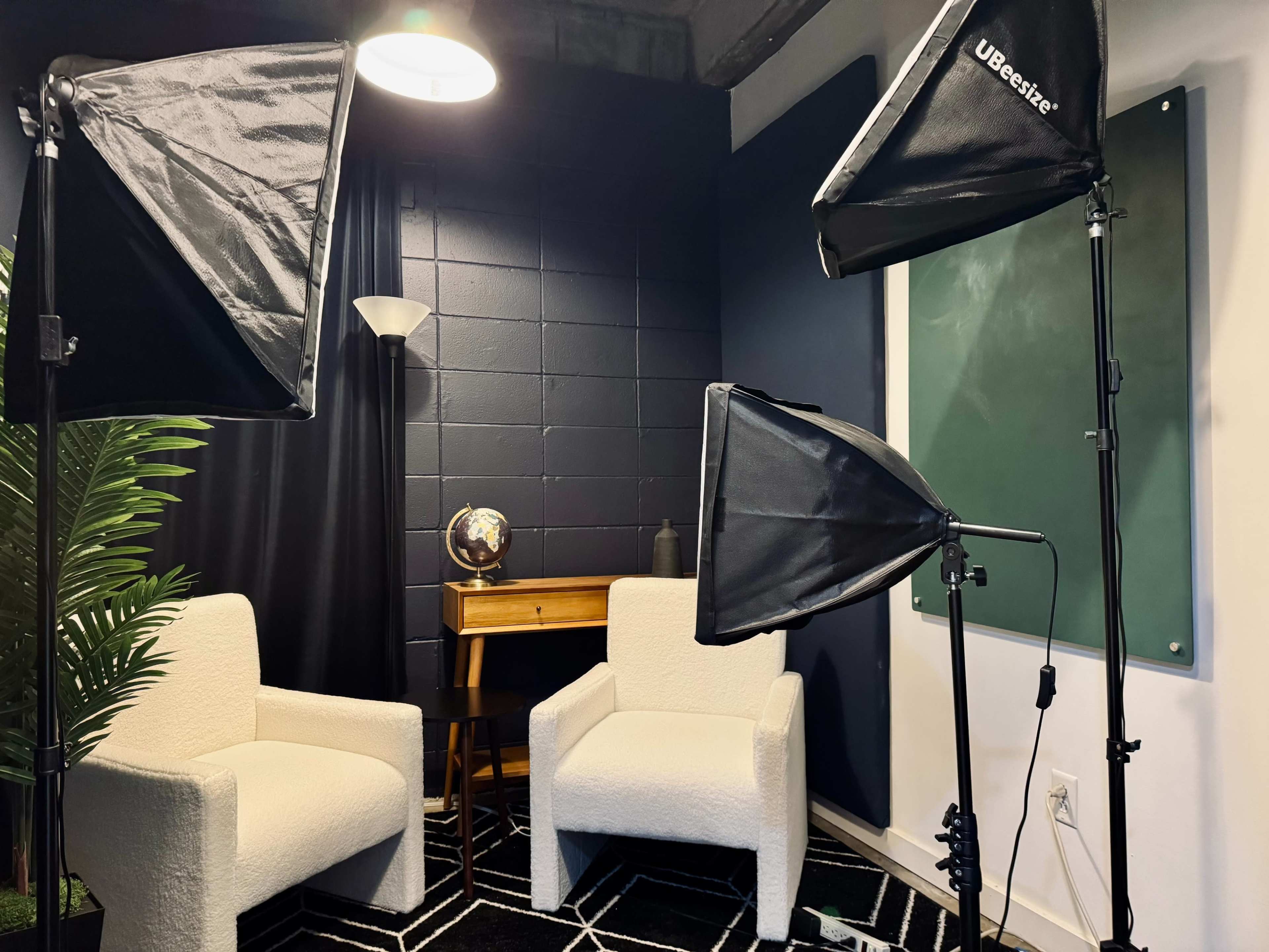 The image shows a small studio setup with two white chairs, a wooden desk, a globe, and multiple light sources illuminating a dark-blue wall.