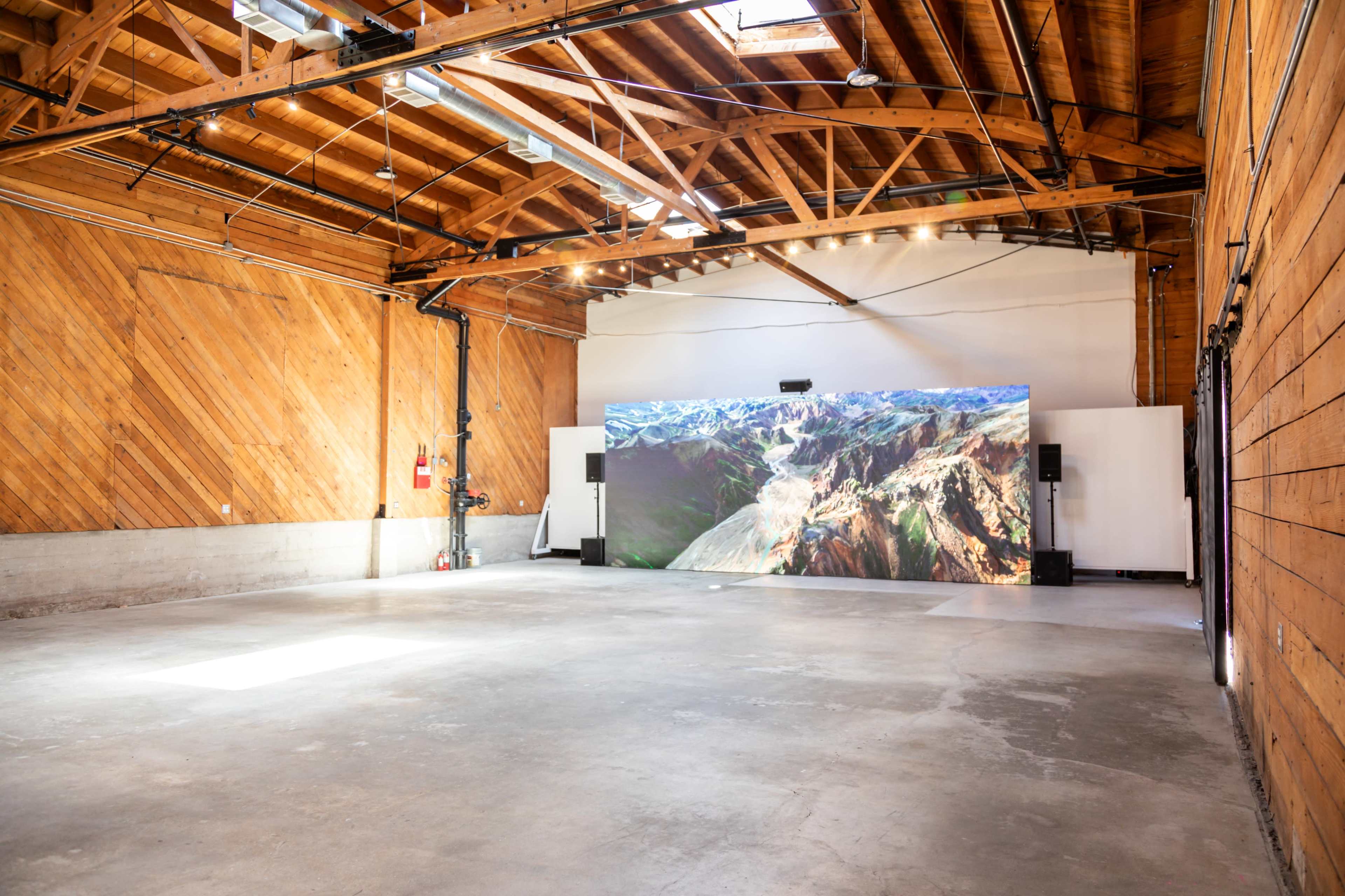 A spacious indoor venue featuring a large screen displaying a mountainous landscape, with wooden walls and a high ceiling.