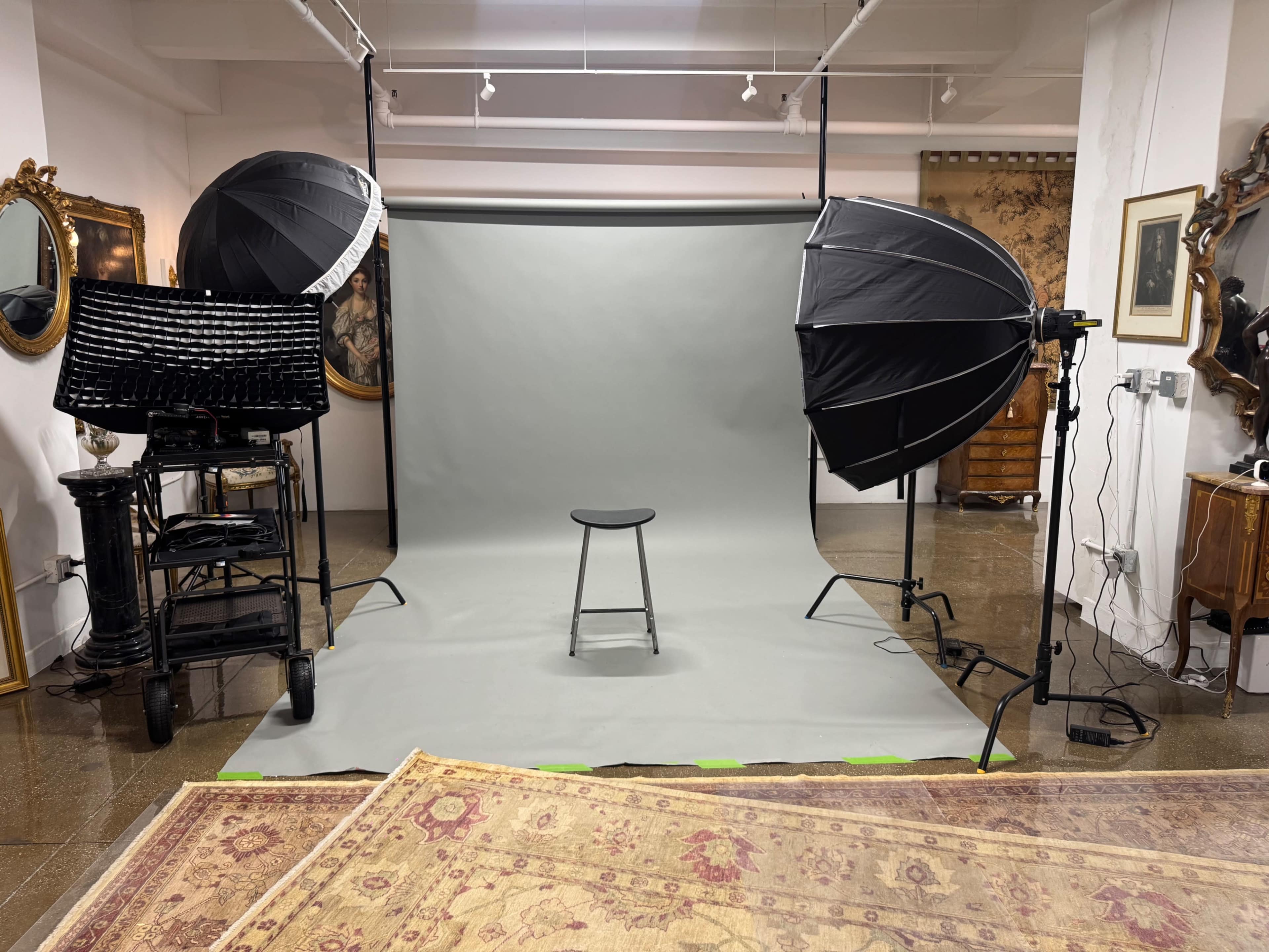 The image shows a photography setup in a studio with a gray backdrop, a stool in the center, and two large softbox lights positioned on either side.