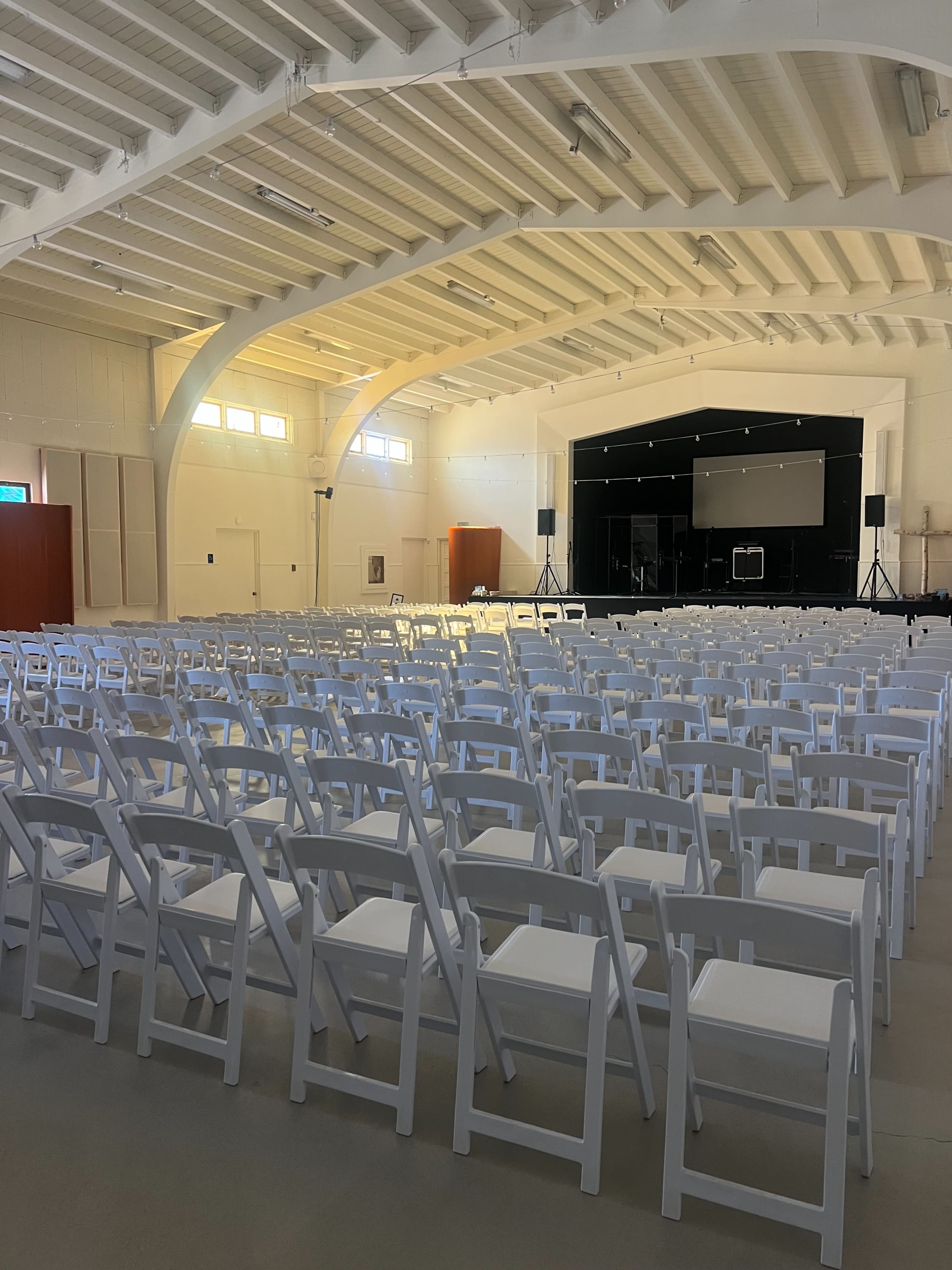 A large event space is set up with rows of white folding chairs facing a stage in the background.