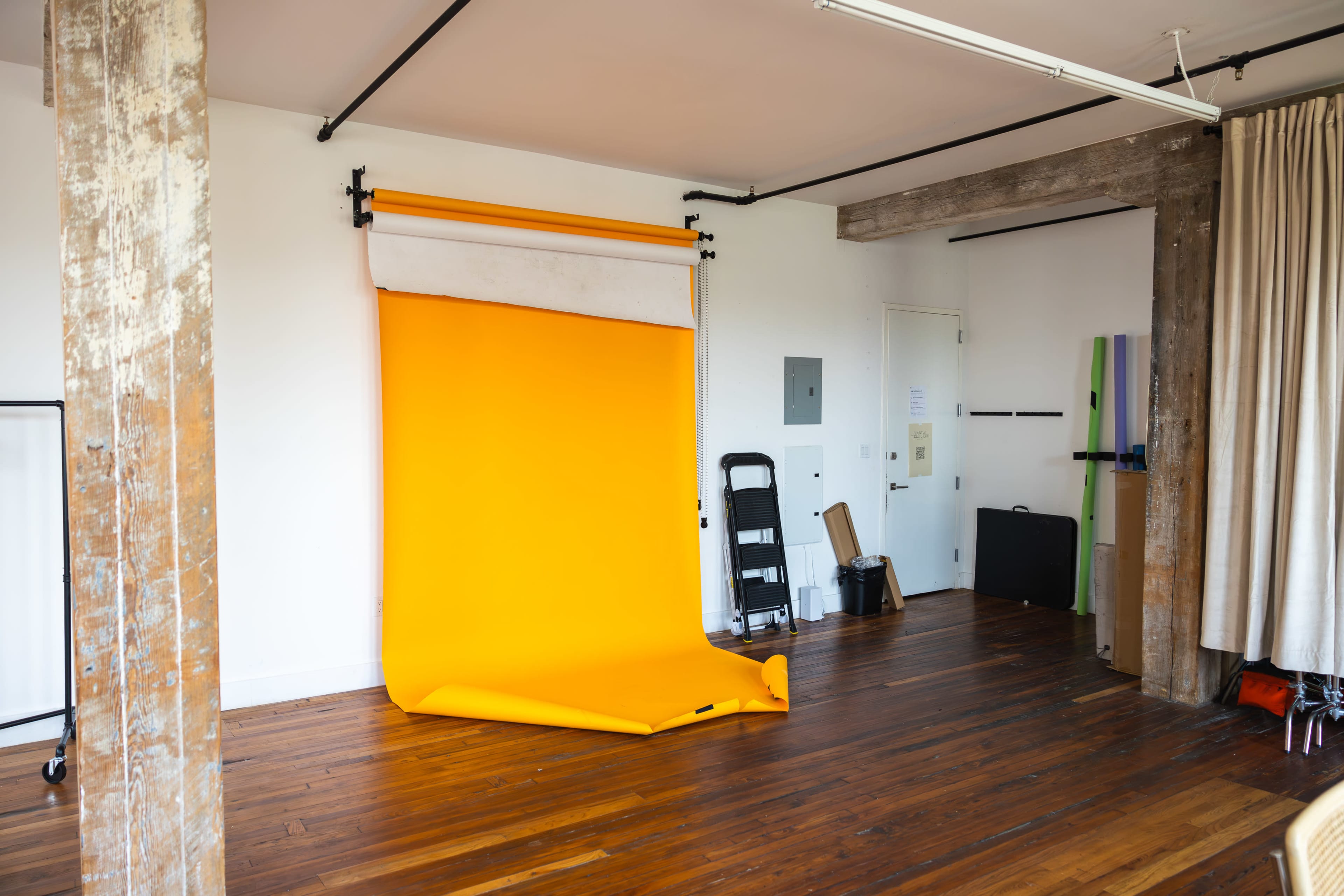 A photography studio with an orange backdrop, wooden floors, and a few pieces of equipment against the walls.