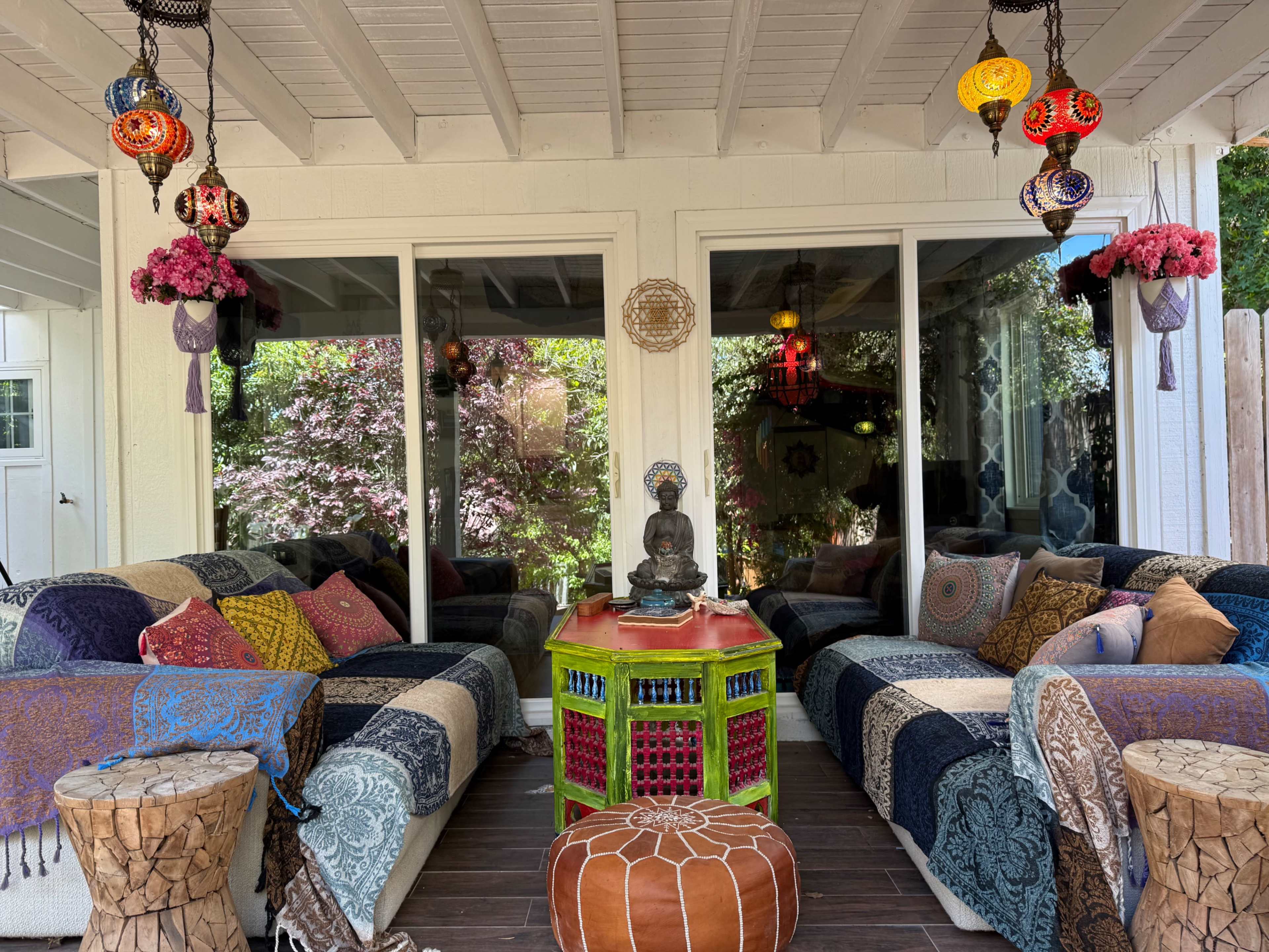 The image shows a cozy outdoor seating area featuring colorful textiles, decorative lanterns, and a statue of Buddha on a vibrant table.