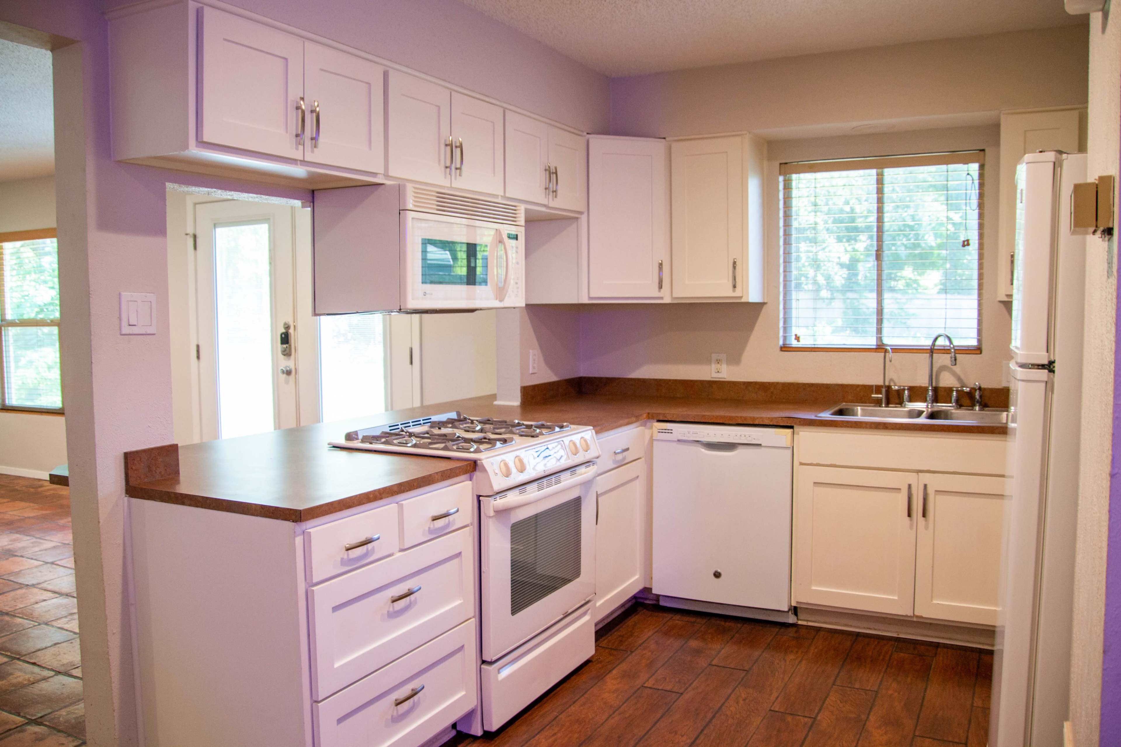 The image shows a modern kitchen with white cabinets, a gas stove, a dishwasher, and a window above the sink.