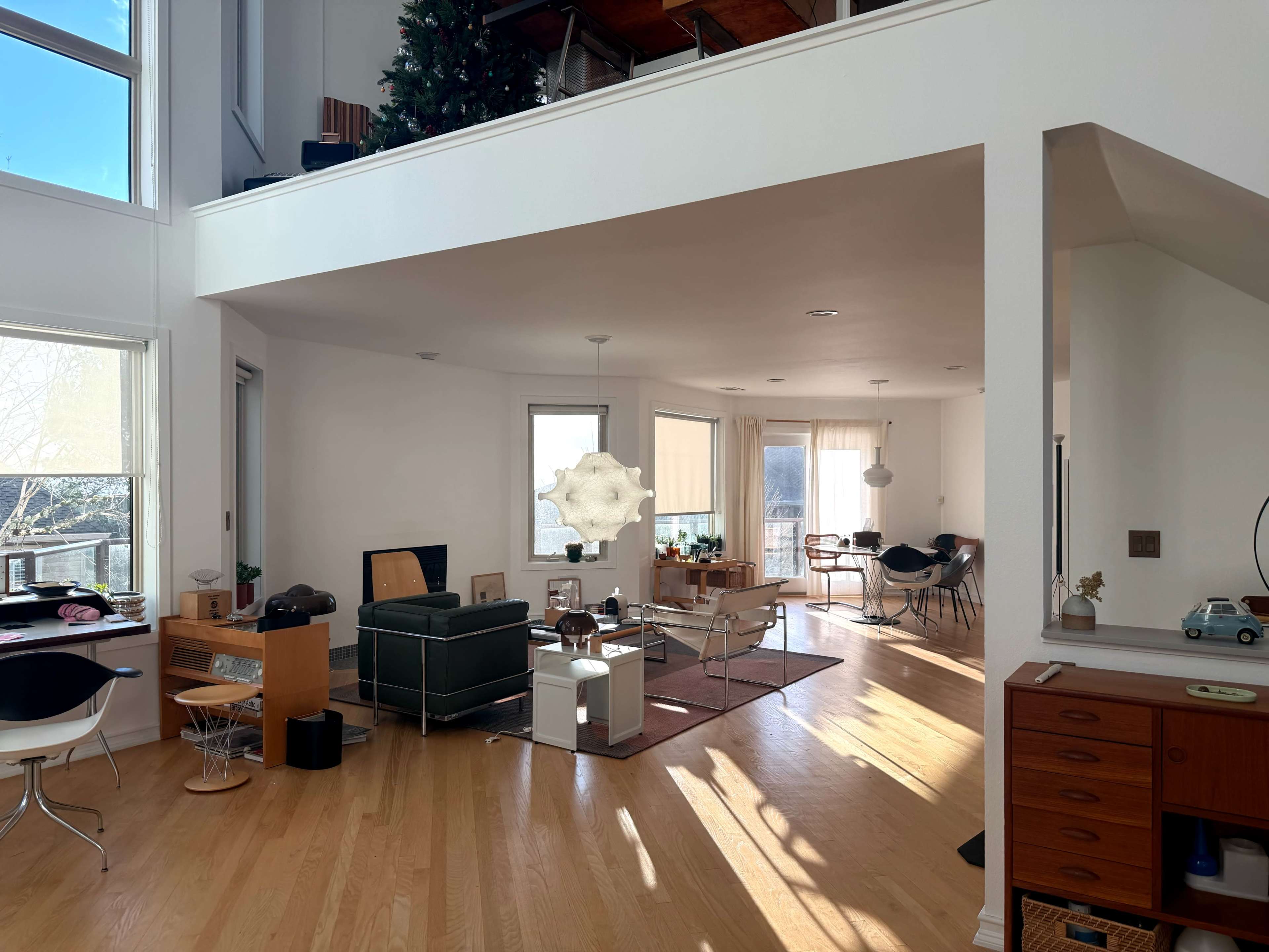 The image shows a modern, open-concept living space with large windows, wooden flooring, and a mix of furniture, including a green sofa and a dining area.