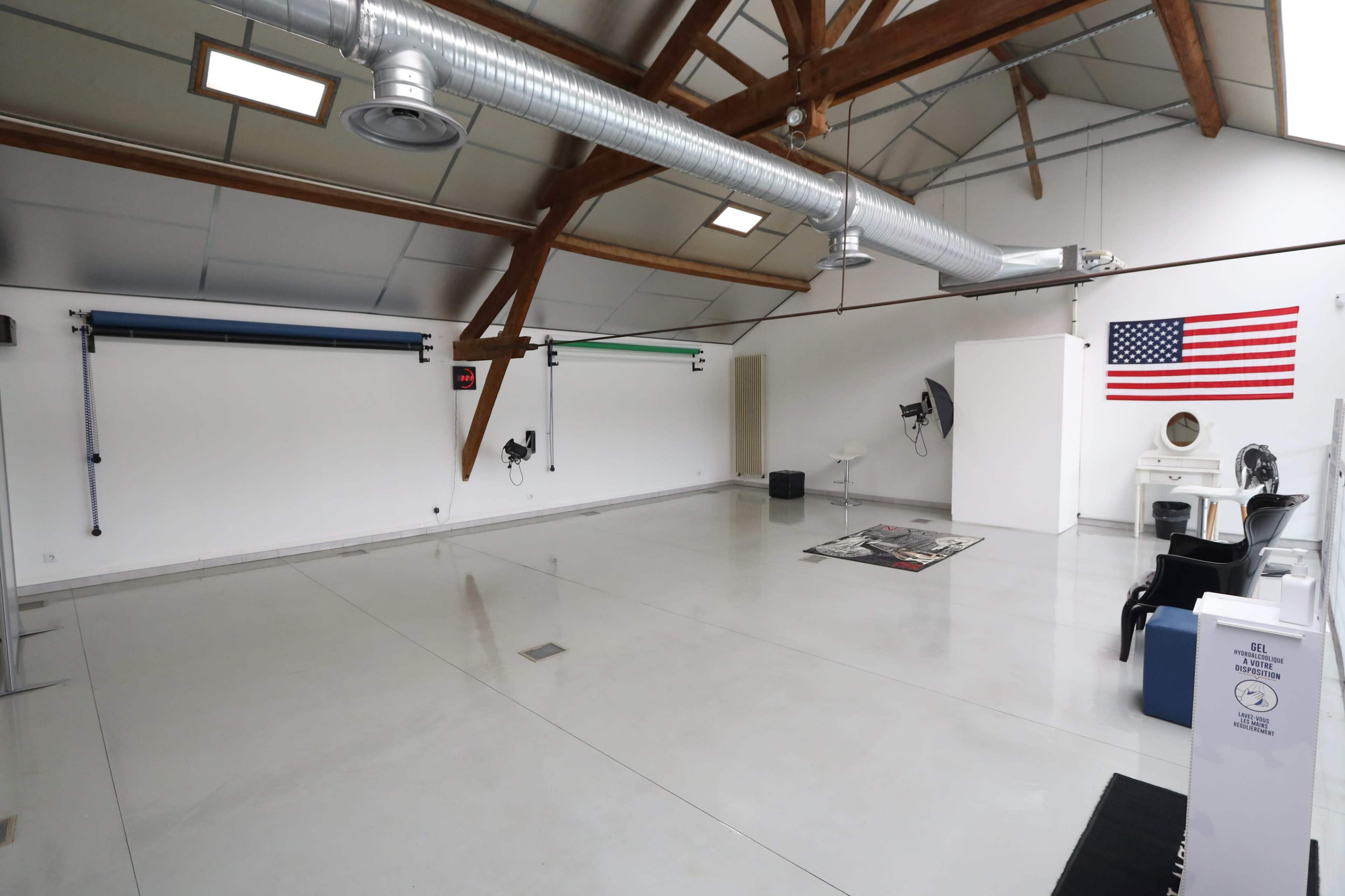 An empty industrial-style room with high ceilings, wooden beams, and various equipment, including a flag and a mirror on the wall.