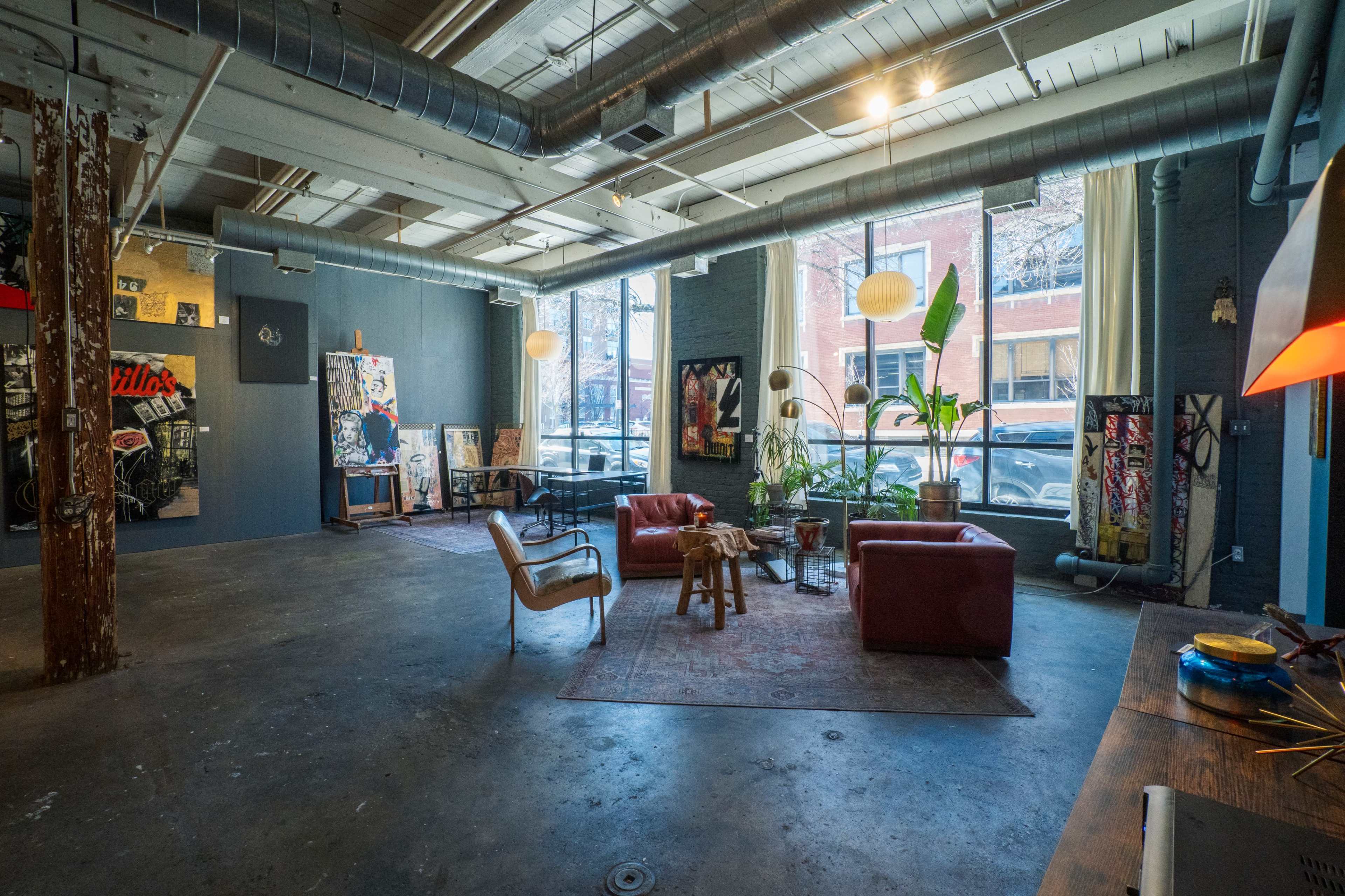 A spacious, industrial-style interior featuring red leather sofas, a wooden table, and various pieces of artwork displayed on the walls.