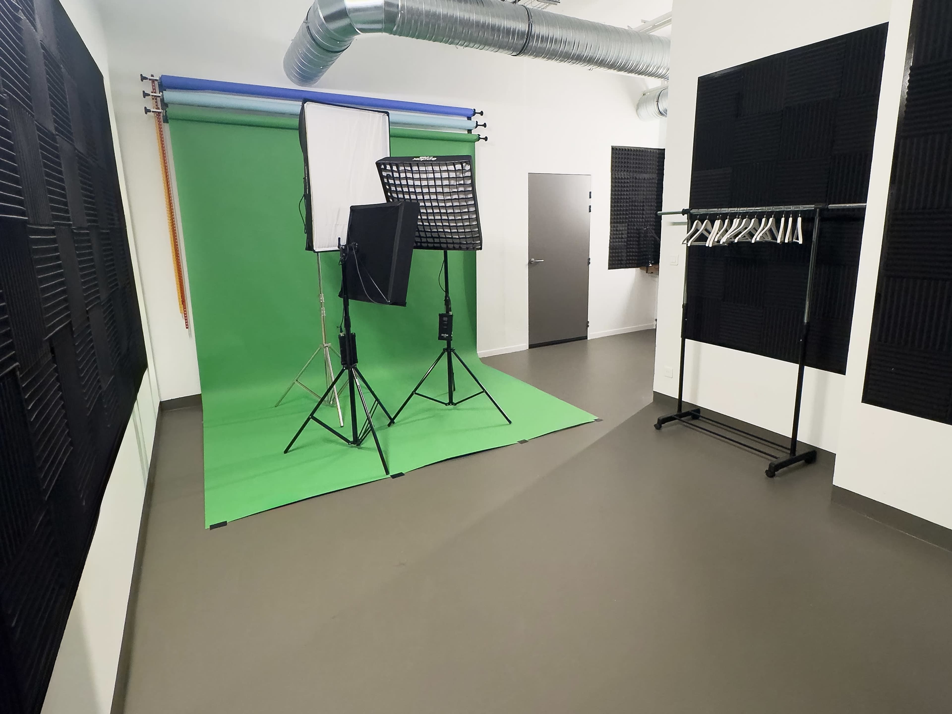 The image shows a photo studio featuring a green backdrop, lighting equipment, and soundproofing panels on the walls.