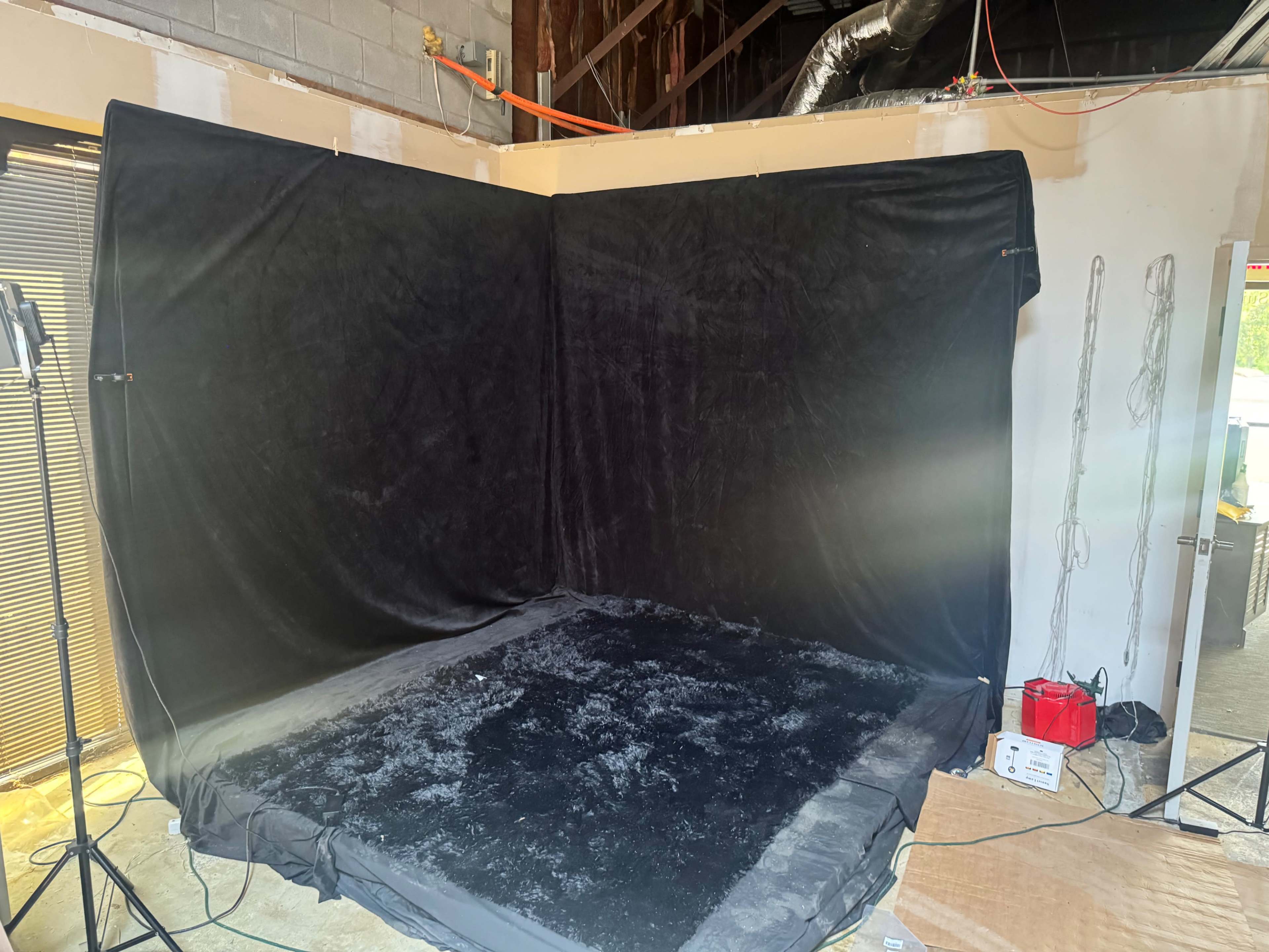 The image shows a black fabric backdrop set up in a studio space with a light source positioned nearby.