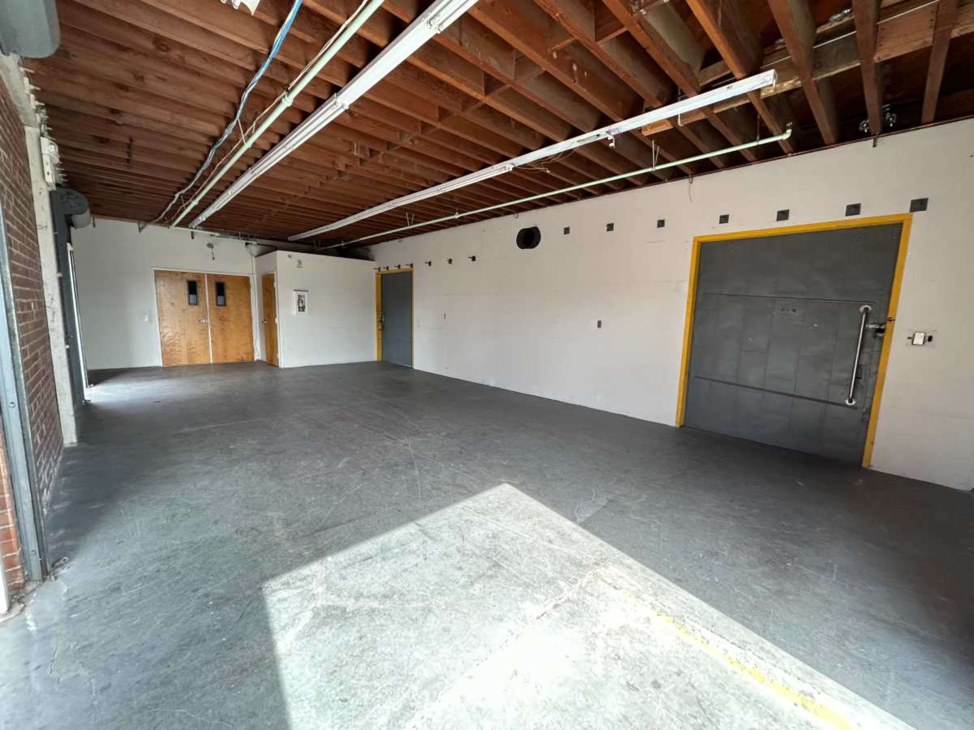 An empty industrial-style room with unfinished walls, exposed ceiling beams, and two large doors.