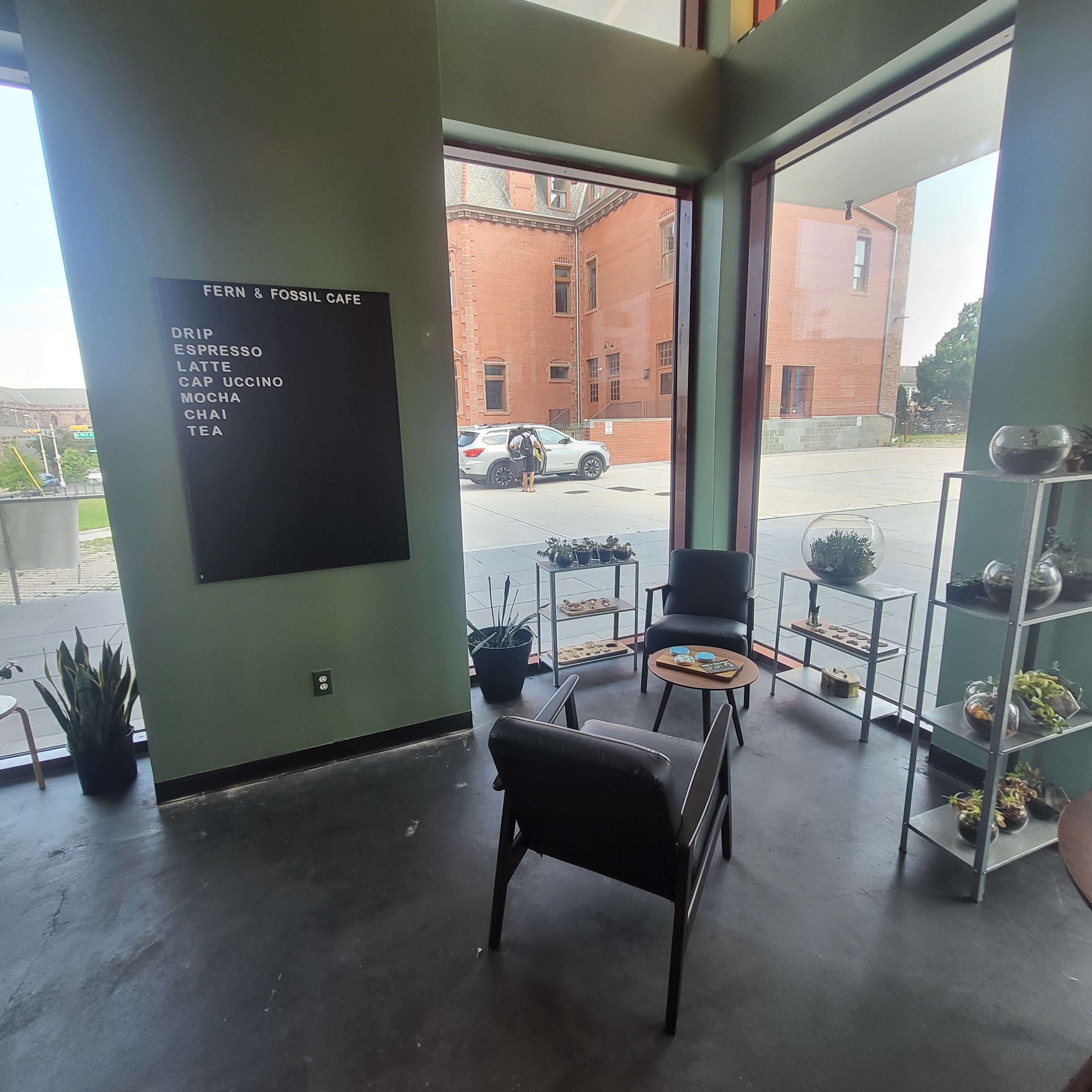 An interior view of a cafe with a menu board, seating area, and large windows overlooking a street.