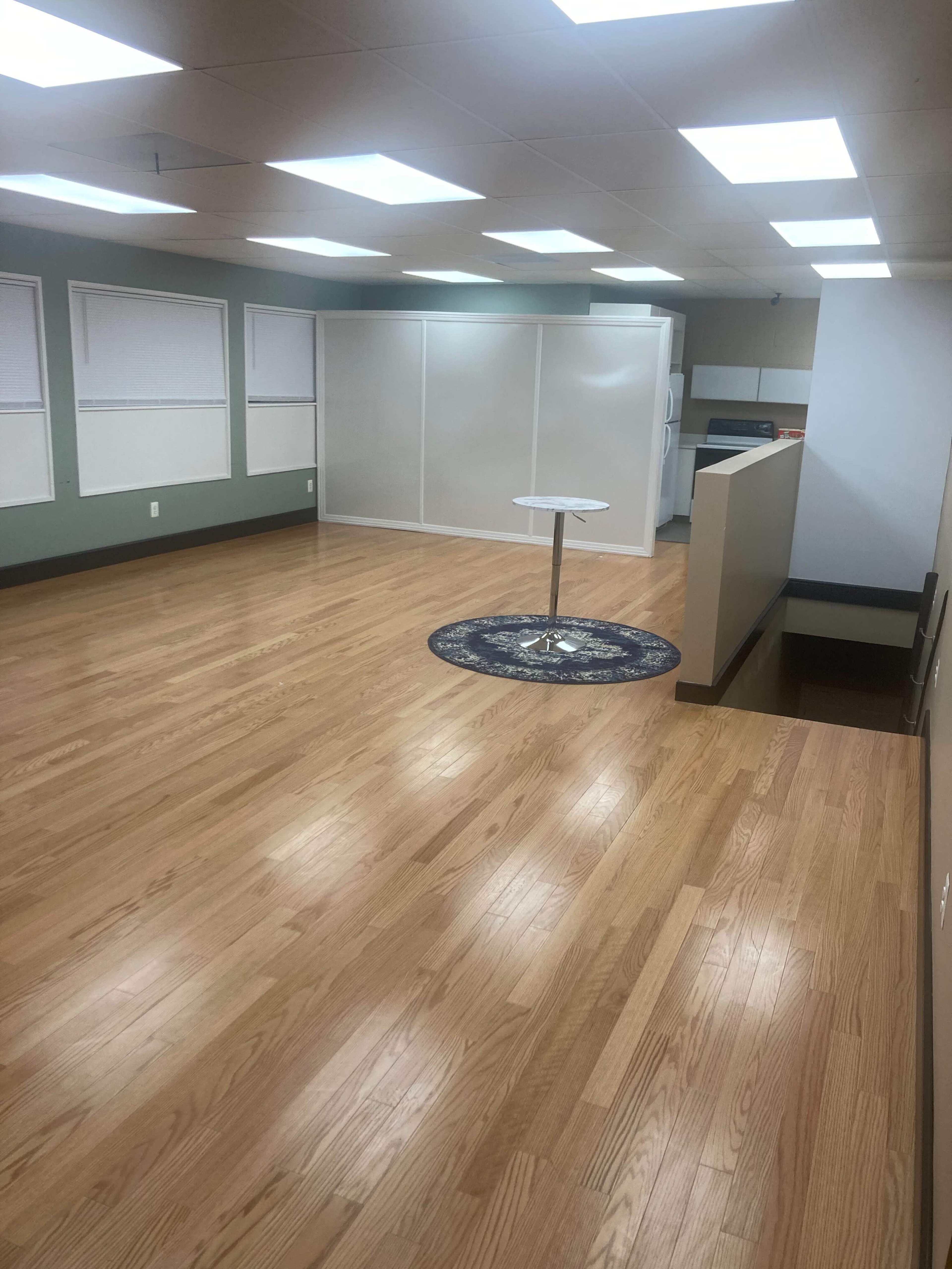 A spacious room with hardwood flooring, large windows, and a central round table on a circular rug.