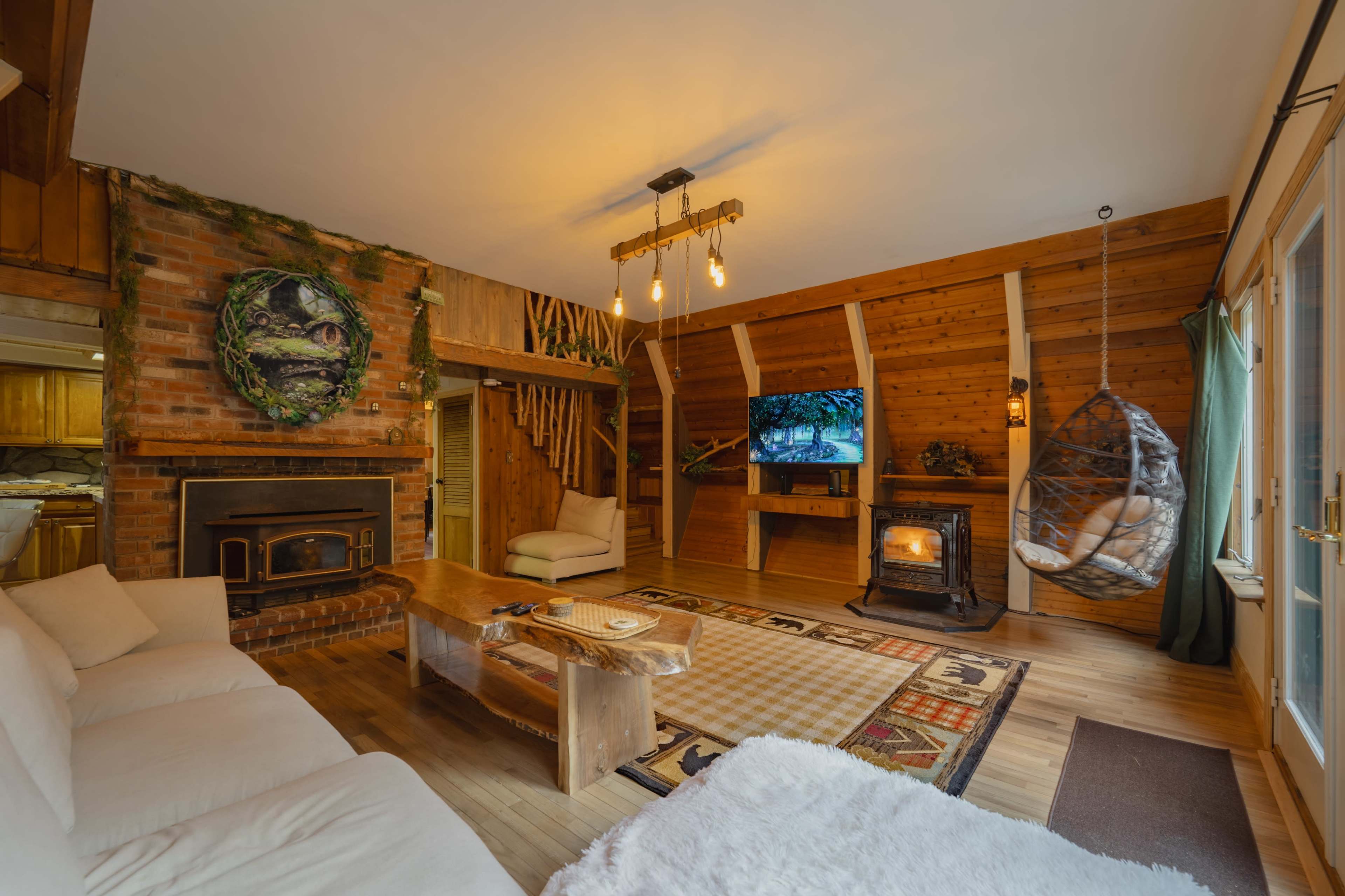 The scene shows a rustic living room with wooden walls, a brick fireplace, a hanging chair, and a television mounted on the wall.