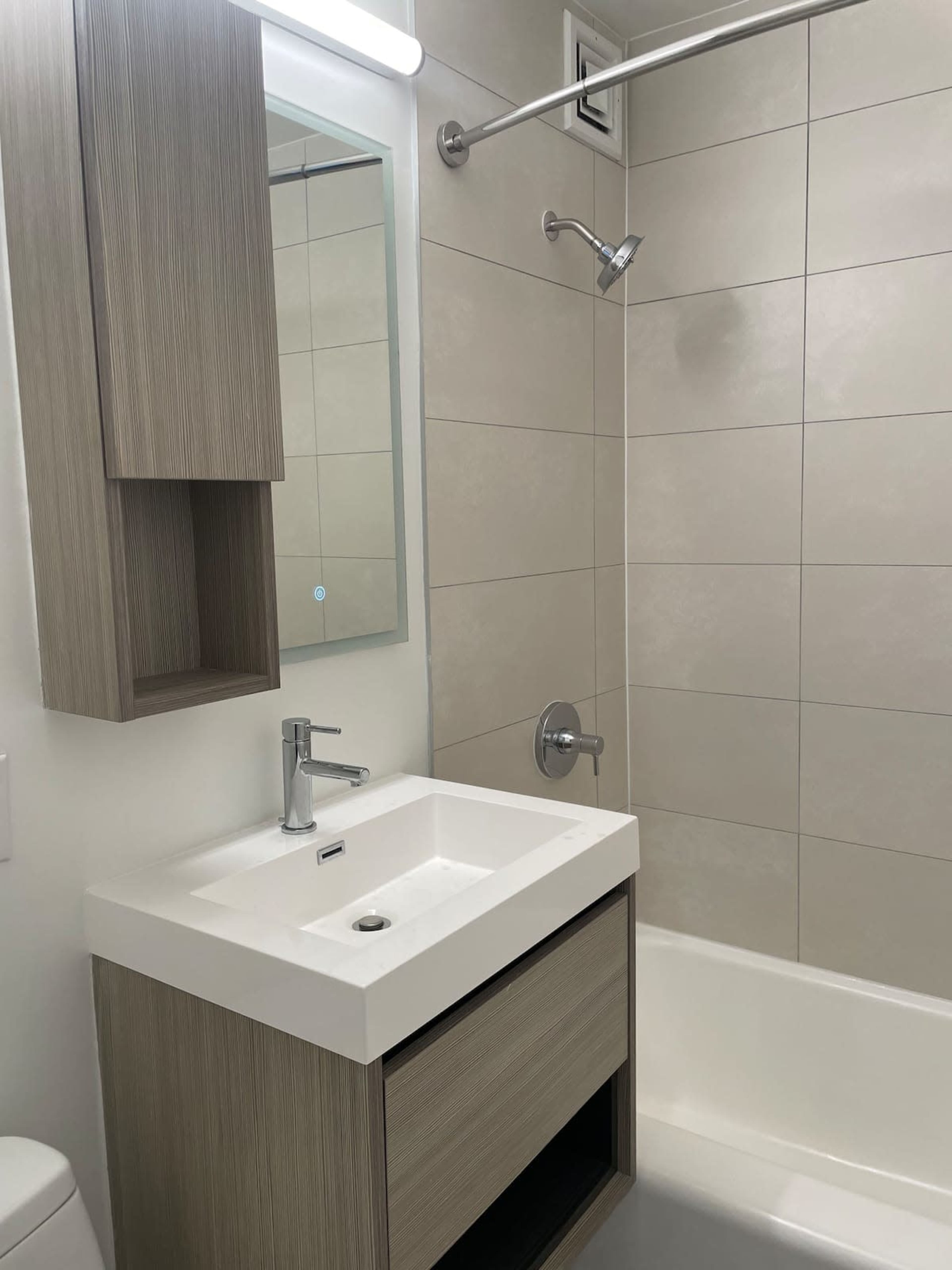 A modern bathroom with a shower, a sink with storage below, and a large wall mirror.