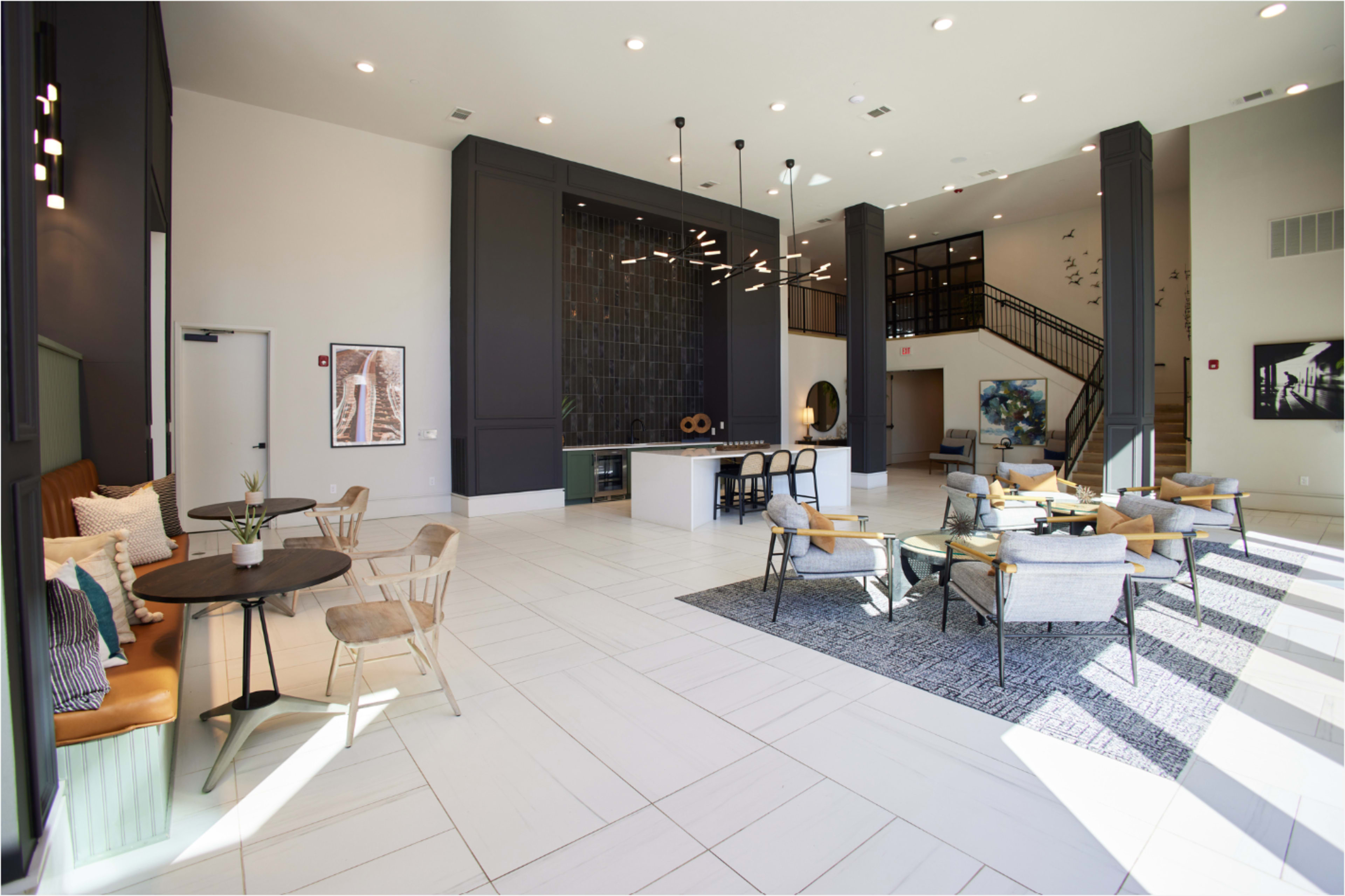 The image shows a spacious modern lobby with a seating area, large windows, and a high ceiling featuring decorative light fixtures.