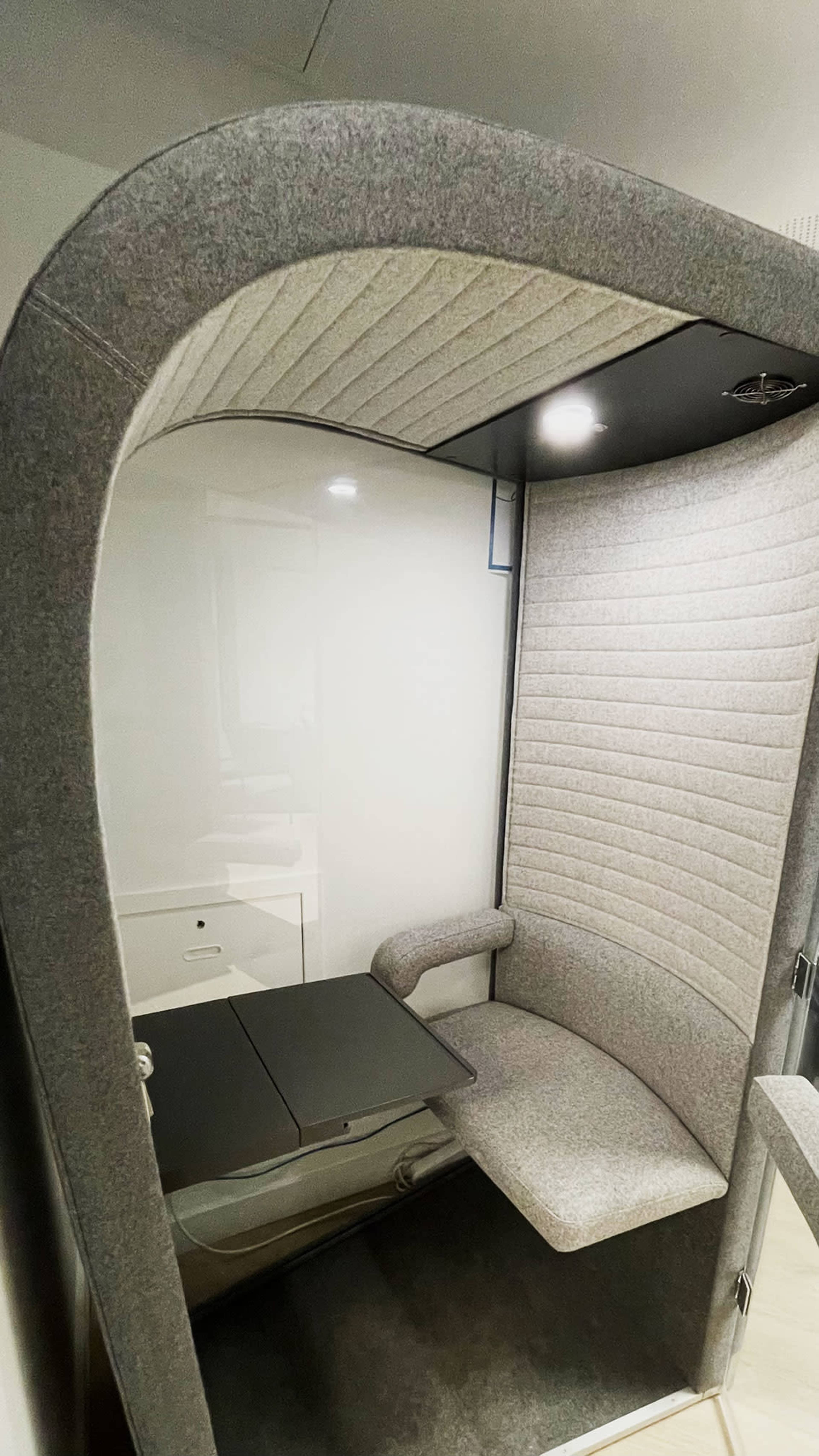 A cozy, enclosed booth with upholstered walls, a small table, and a single chair, designed for privacy and focused work.