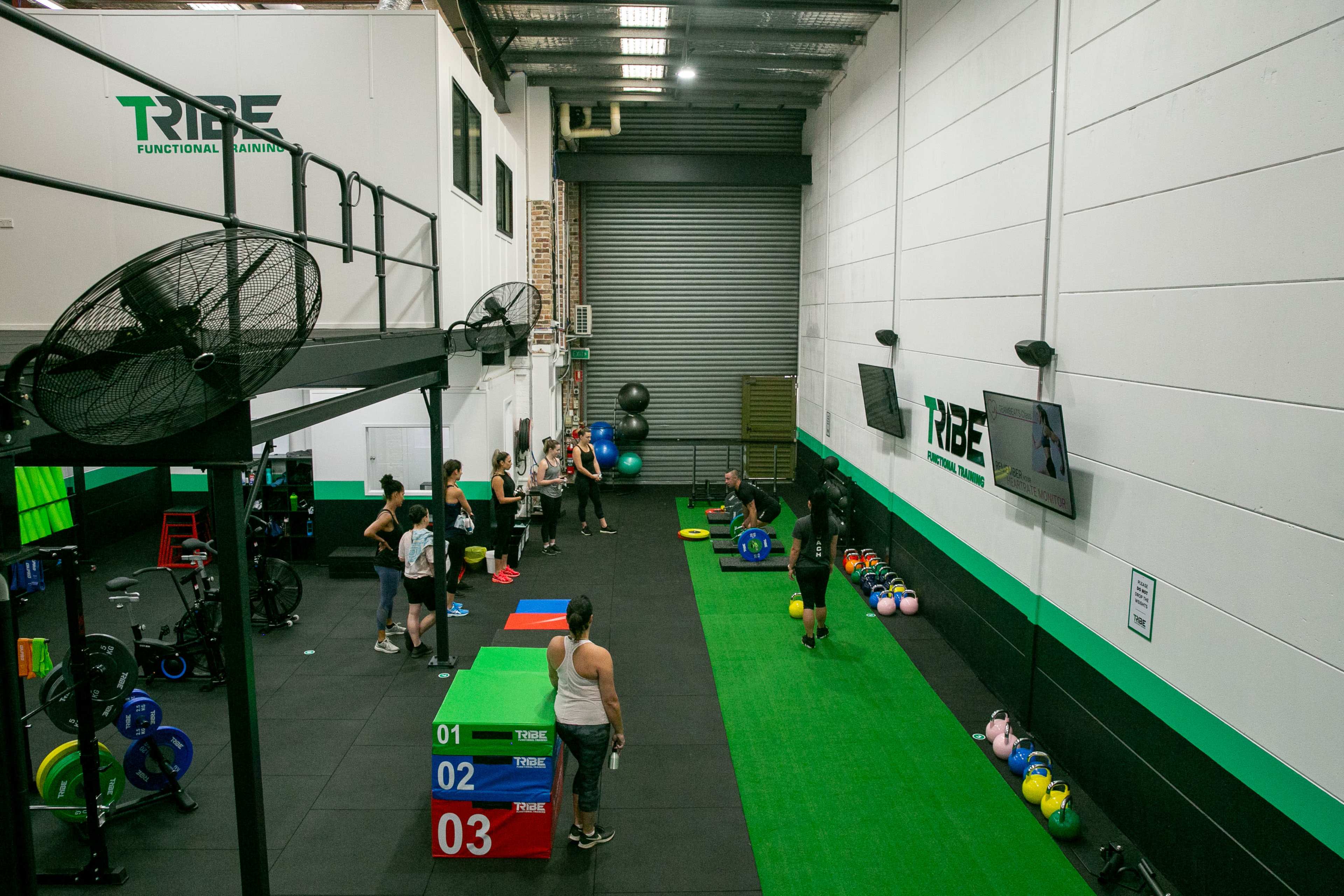 A fitness training facility with various exercise equipment, colored boxes, and individuals participating in a workout session.