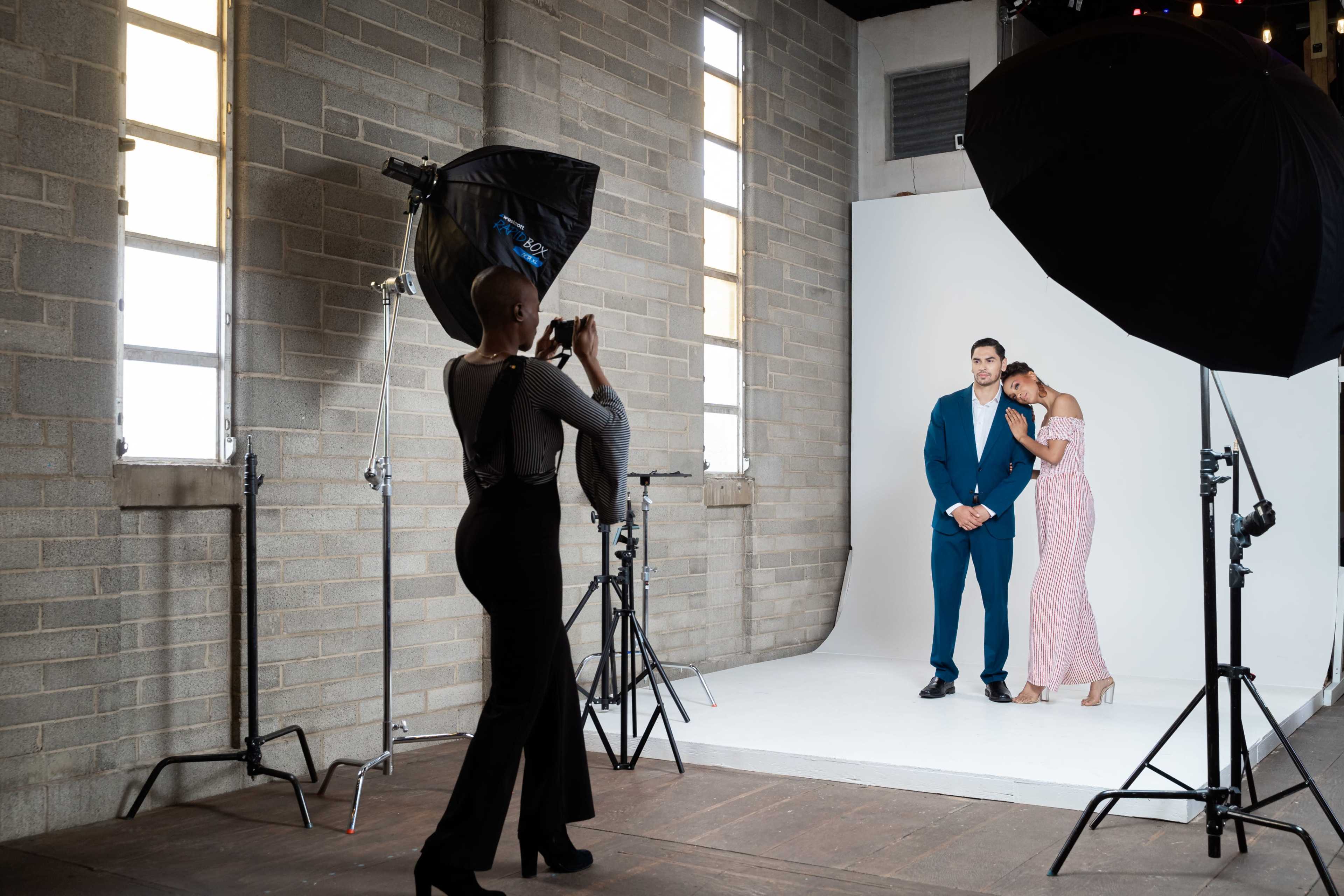 A photographer captures a couple posing in front of a backdrop in a well-lit studio with large softbox lights.