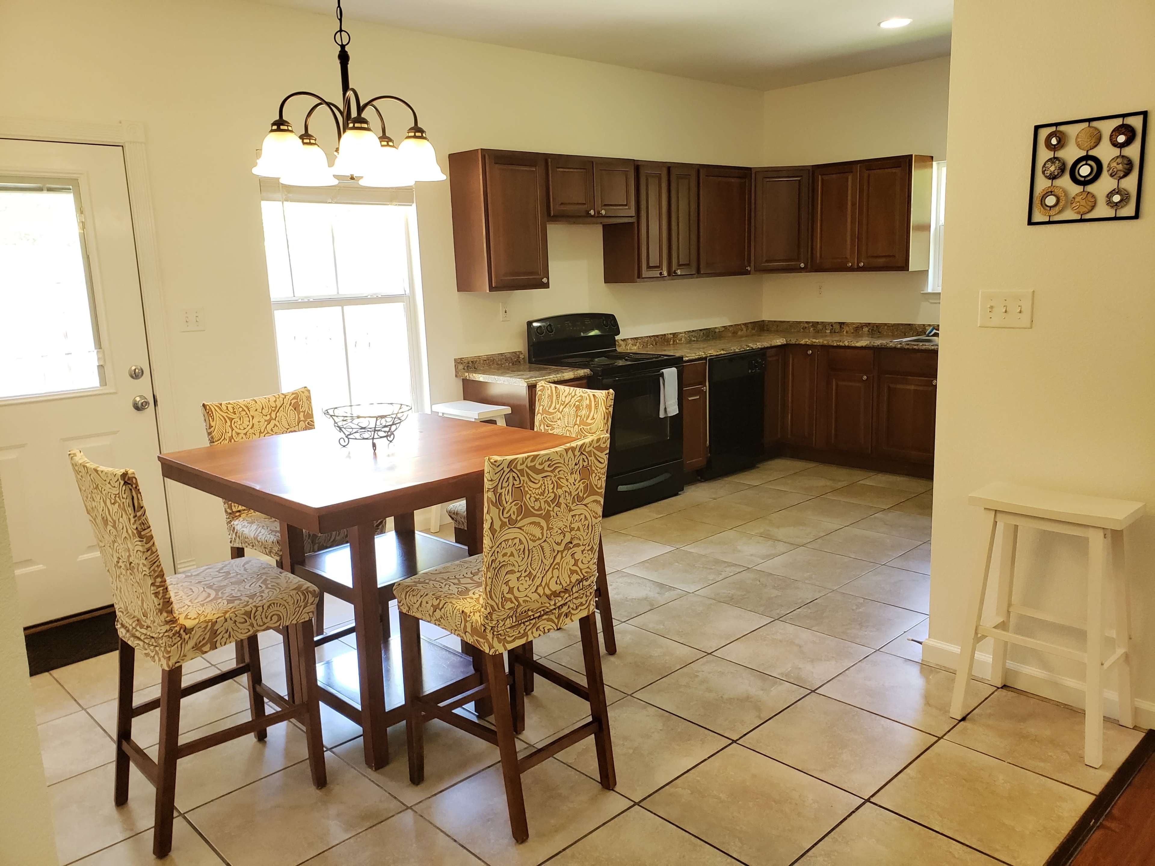 A kitchen with dark wooden cabinets, a black stove, and a table surrounded by four chairs, positioned on a tiled floor.